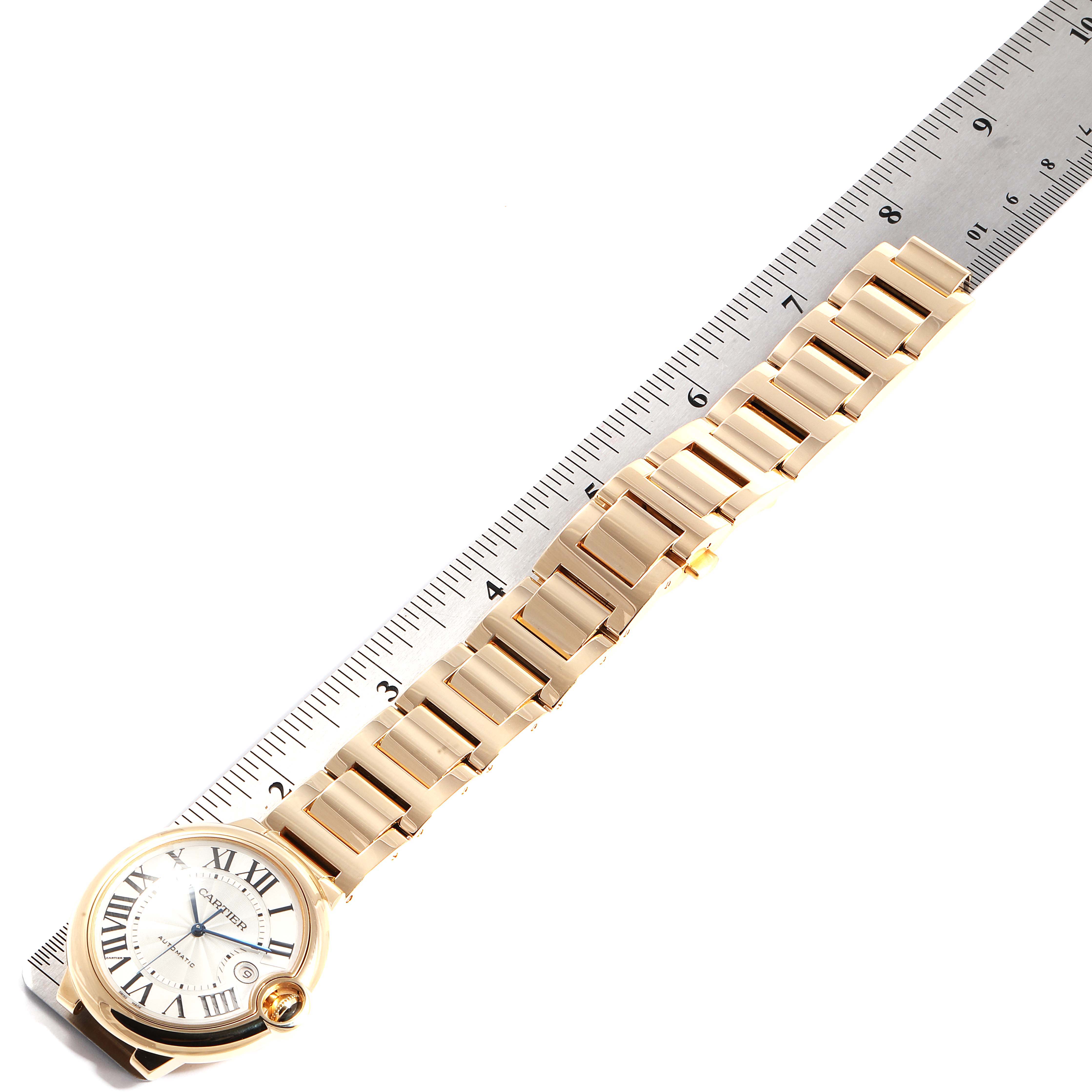 The image shows the Cartier Ballon Bleu W69005Z2  Men's Yellow Gold Silver Dial W69005Z2  Men's Yellow Gold Silver Dial watch laid flat alongside a measuring ruler, displaying its dial and full gold bracelet.
