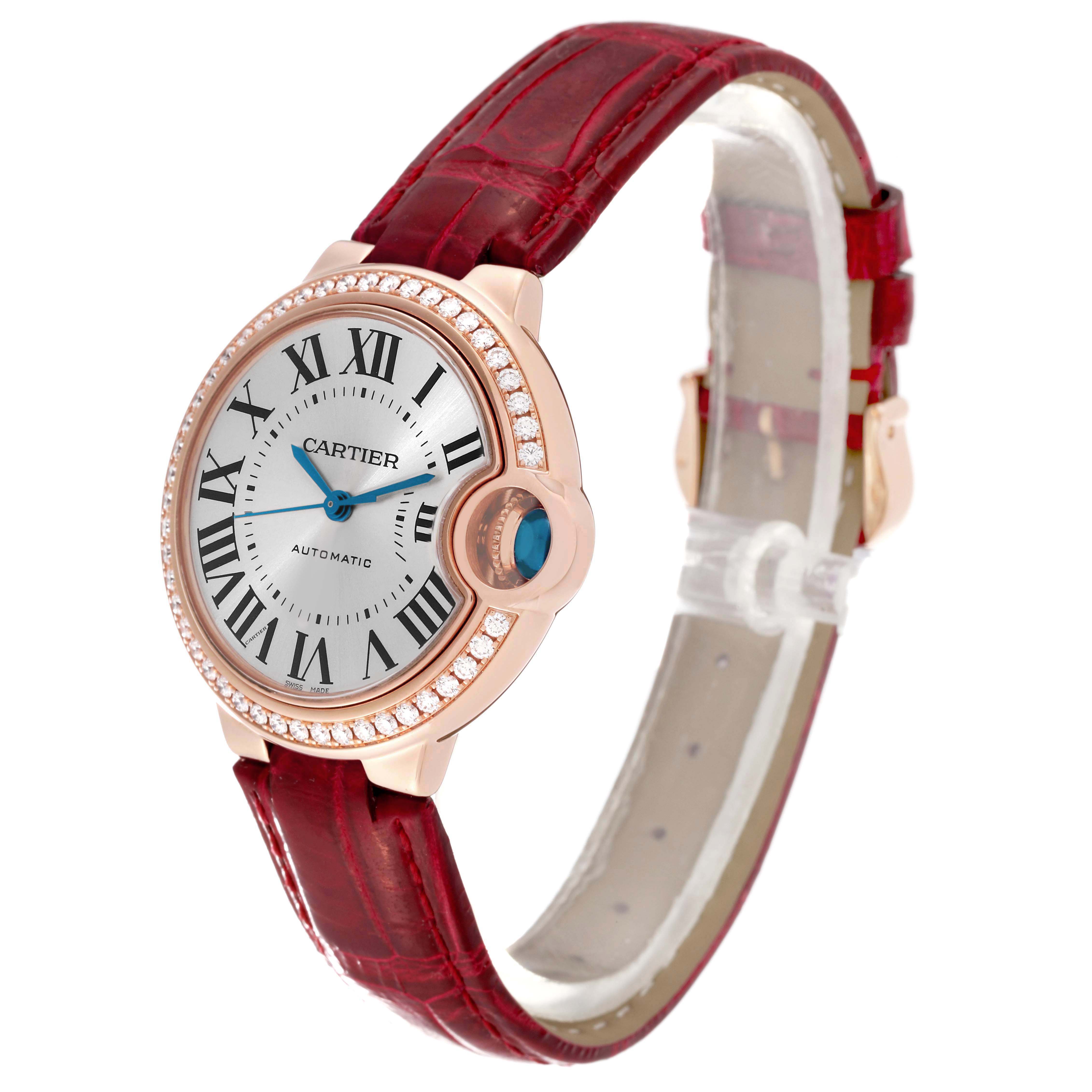 The Cartier Ballon Bleu WJBB0033 Women's Rose Gold Silver Dial watch is shown at a side angle, highlighting its round face, diamond bezel, blue cabochon crown, and red strap.