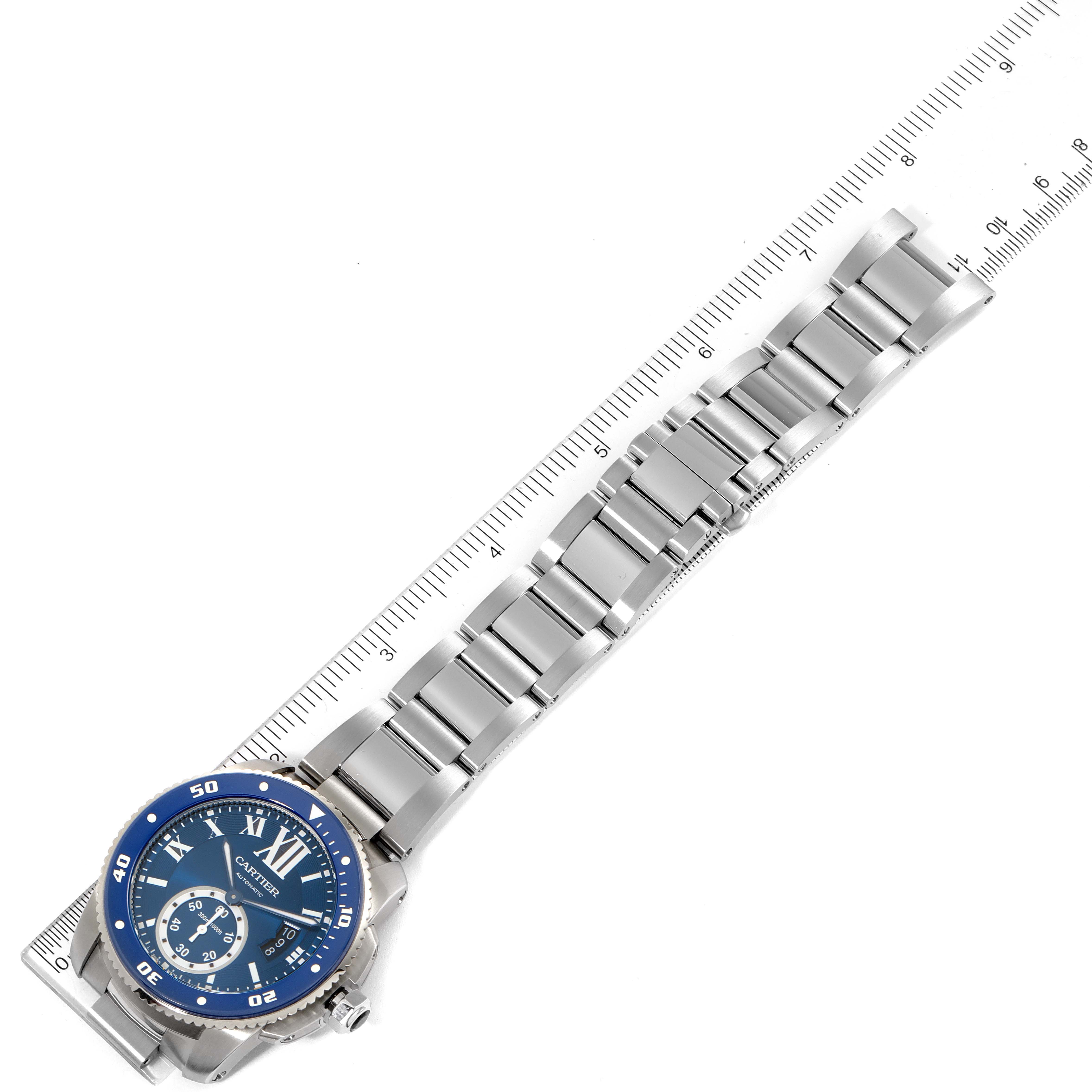 This image shows a top-down view of a Calibre de Cartier model by Cartier, displaying the blue dial and metal strap alongside a ruler.