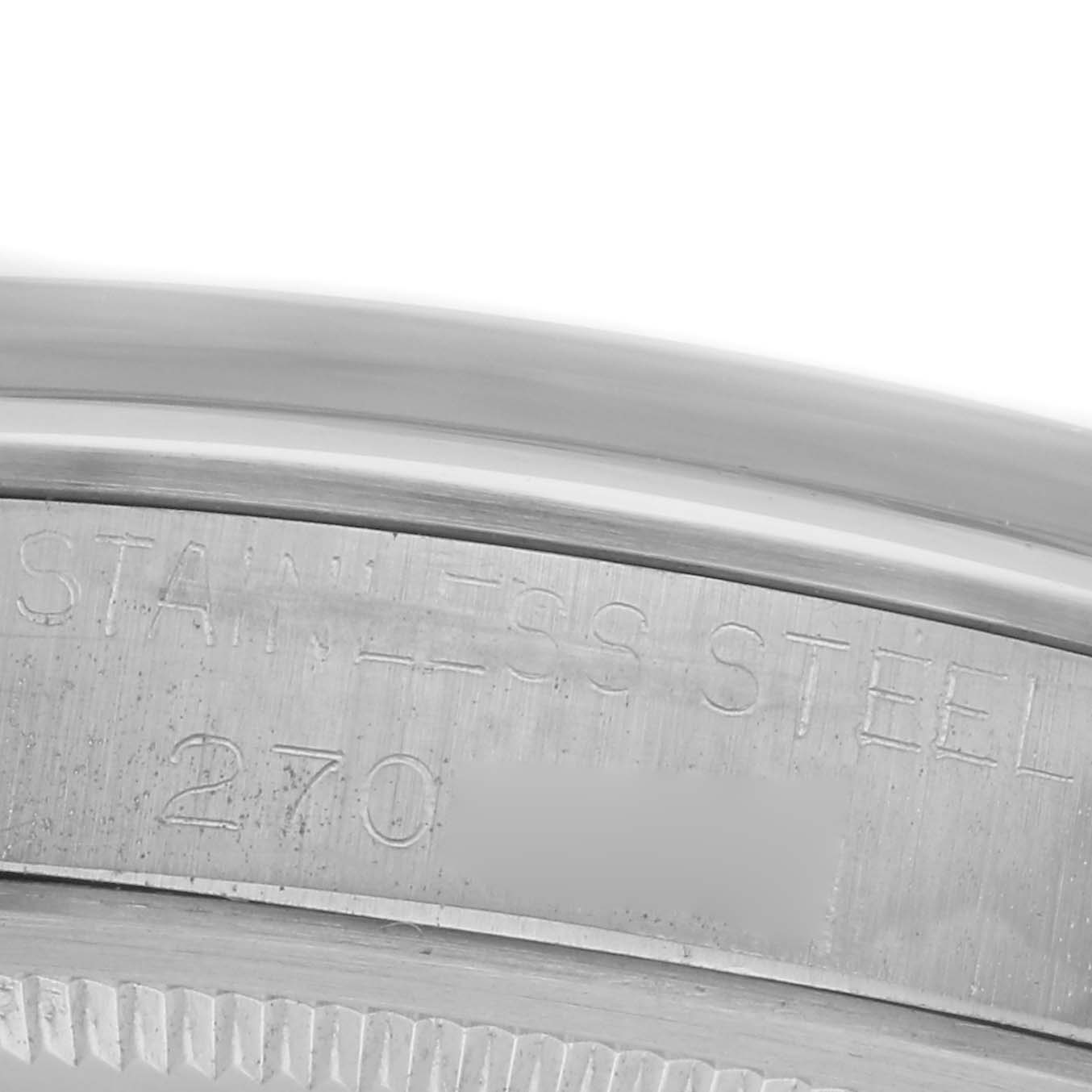The image shows a close-up of the Rolex Date model's rim, featuring "Stainless Steel" engraving and partial reference numbers.