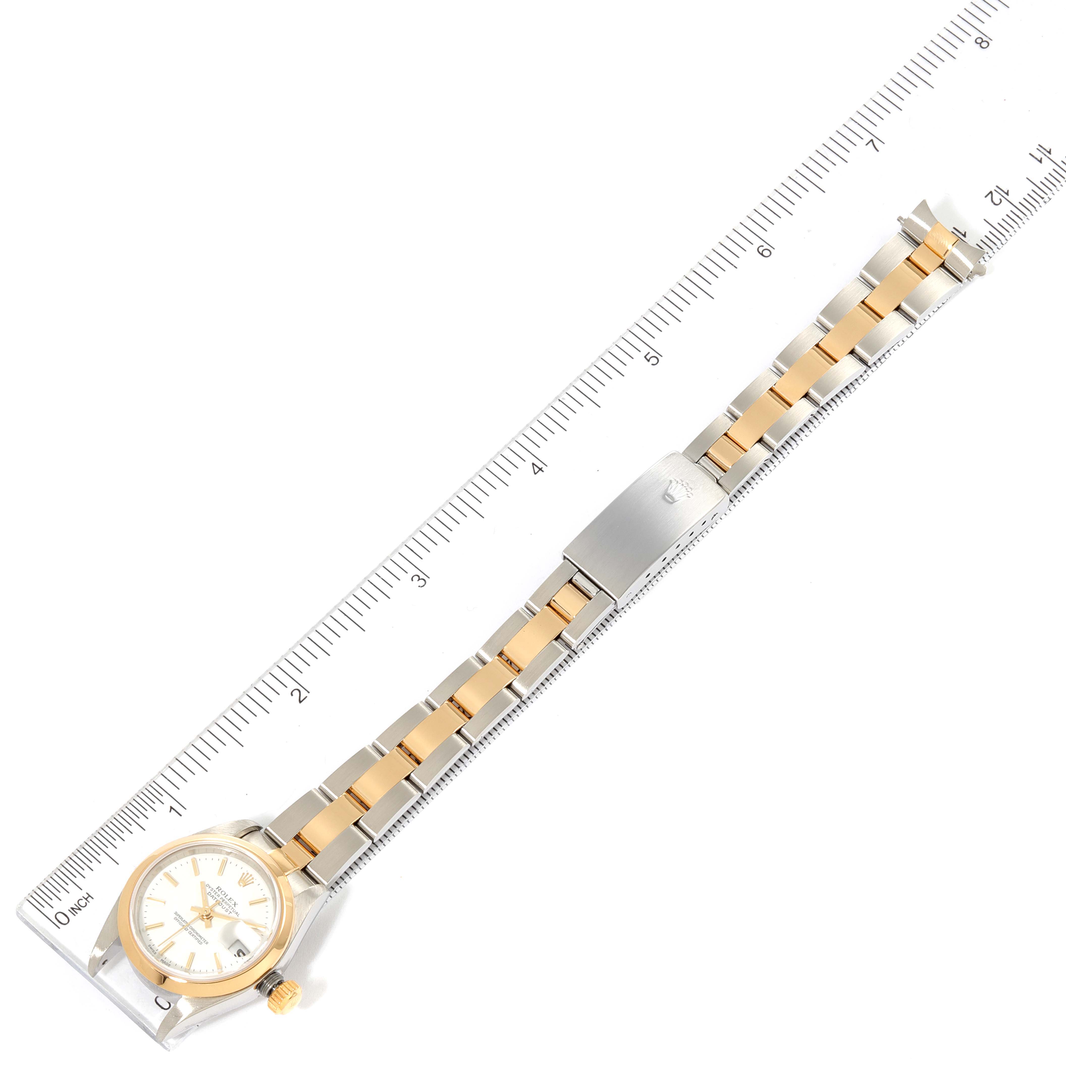 The Rolex Datejust 79163 Women's Steel and Gold (two tone) White Dial 79163 Women's Steel and Gold (two tone) White Dial watch is shown from a top-down angle, displaying its face and full metal strap alongside a ruler for scale.