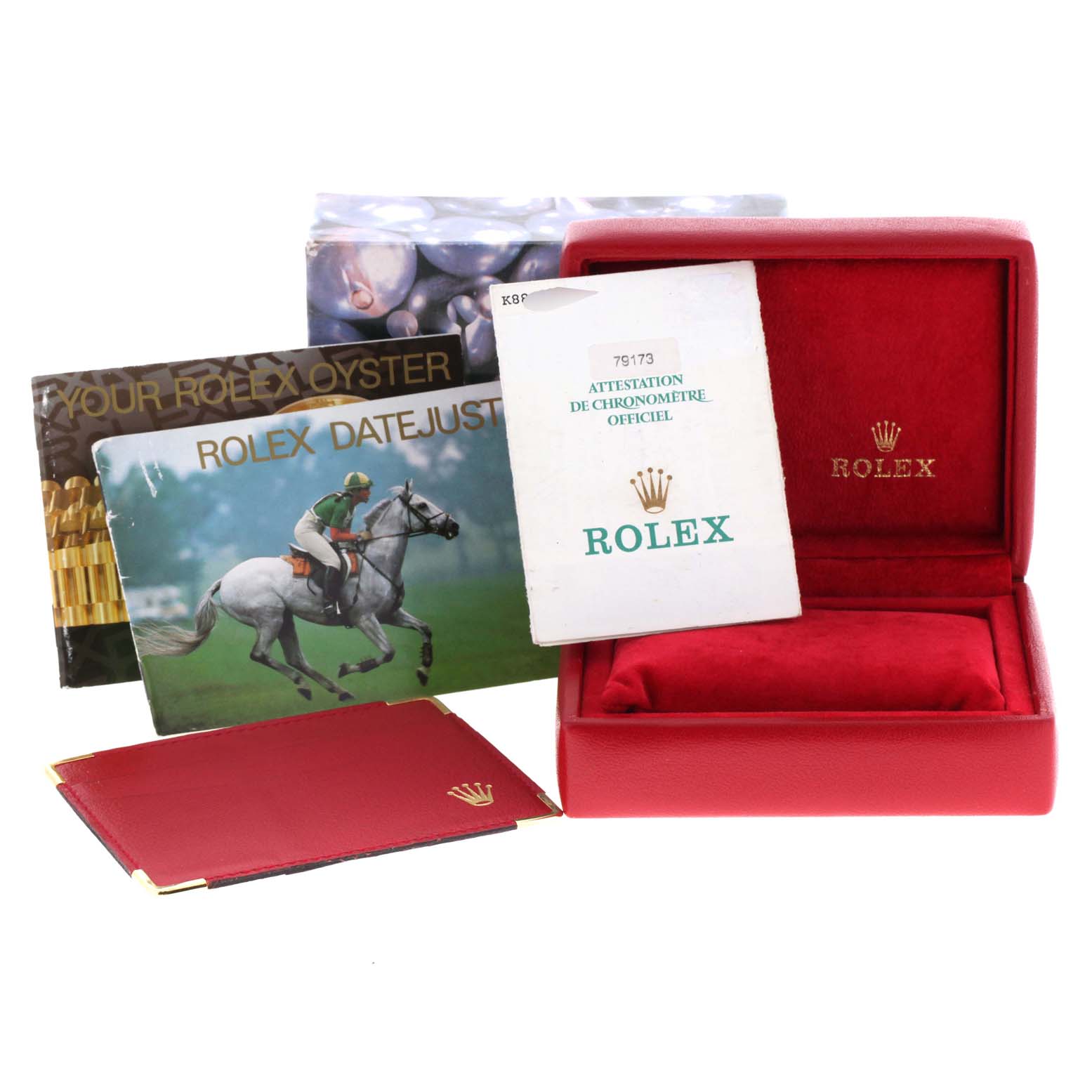 The image shows a red Rolex Datejust 79173 Women
s Steel and Gold (two tone) White Dial 79173 Women
s Steel and Gold (two tone) White Dial box, a red holder, booklets, and certification papers from a frontal angle.