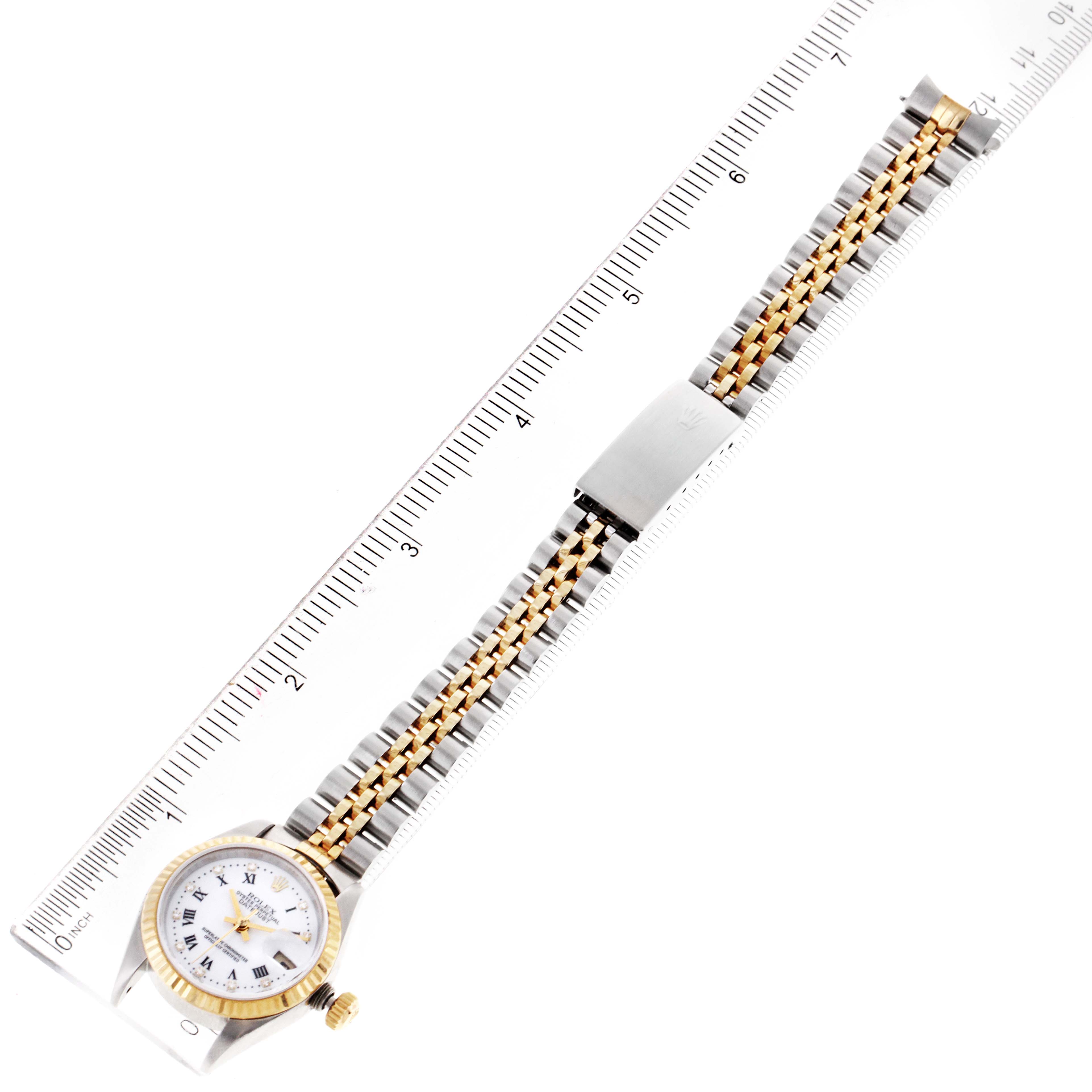 This image shows a Rolex Datejust 79173 Women
s Steel and Gold (two tone) White Dial 79173 Women
s Steel and Gold (two tone) White Dial watch at an overhead angle, displaying its dial, bezel, and bracelet against a ruler.