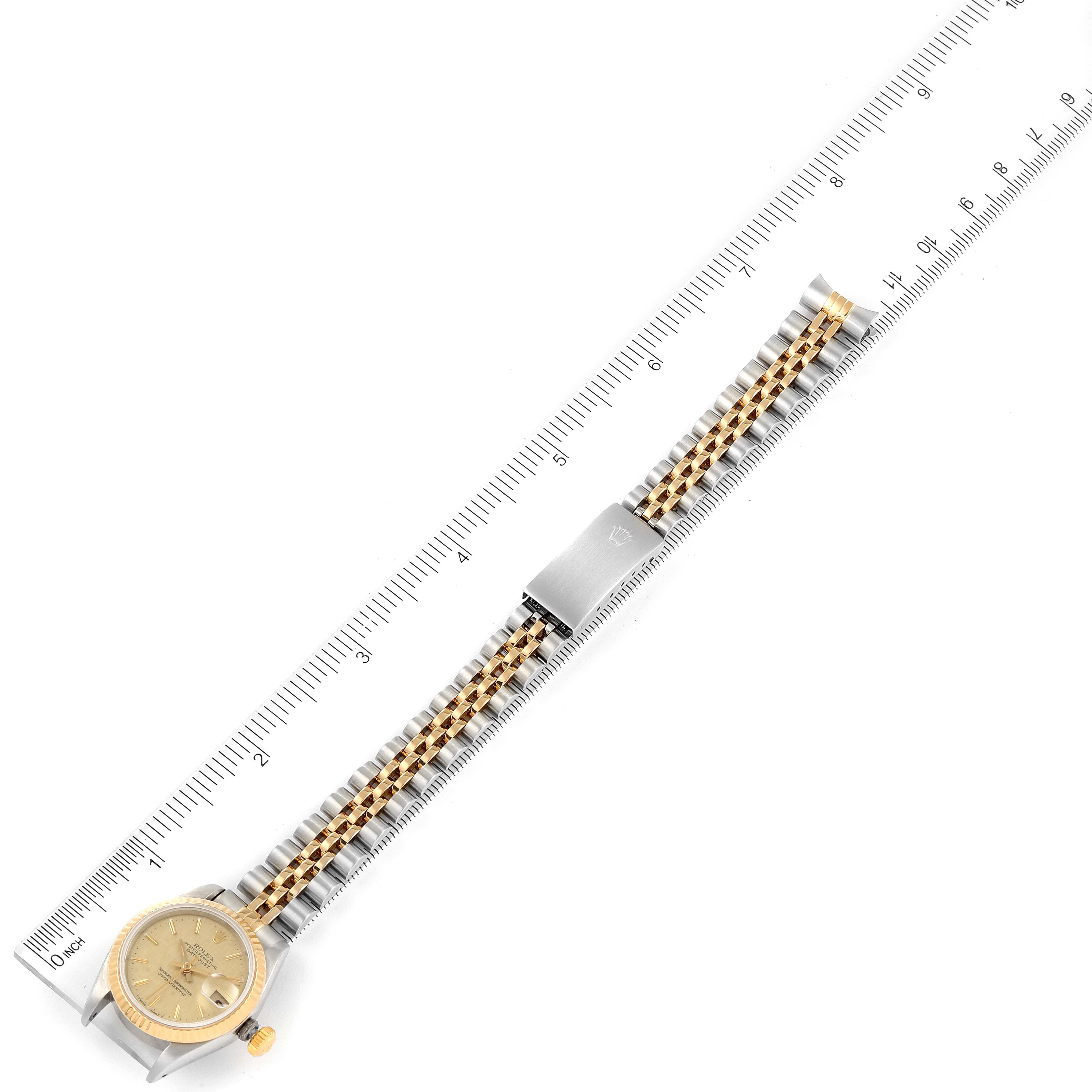 This image shows a full view of a Rolex Datejust 69173 Women
s Steel and Gold (two tone) Champagne Dial 69173 Women
s Steel and Gold (two tone) Champagne Dial model, highlighting the dial, bracelet, and clasp, placed against a ruler.