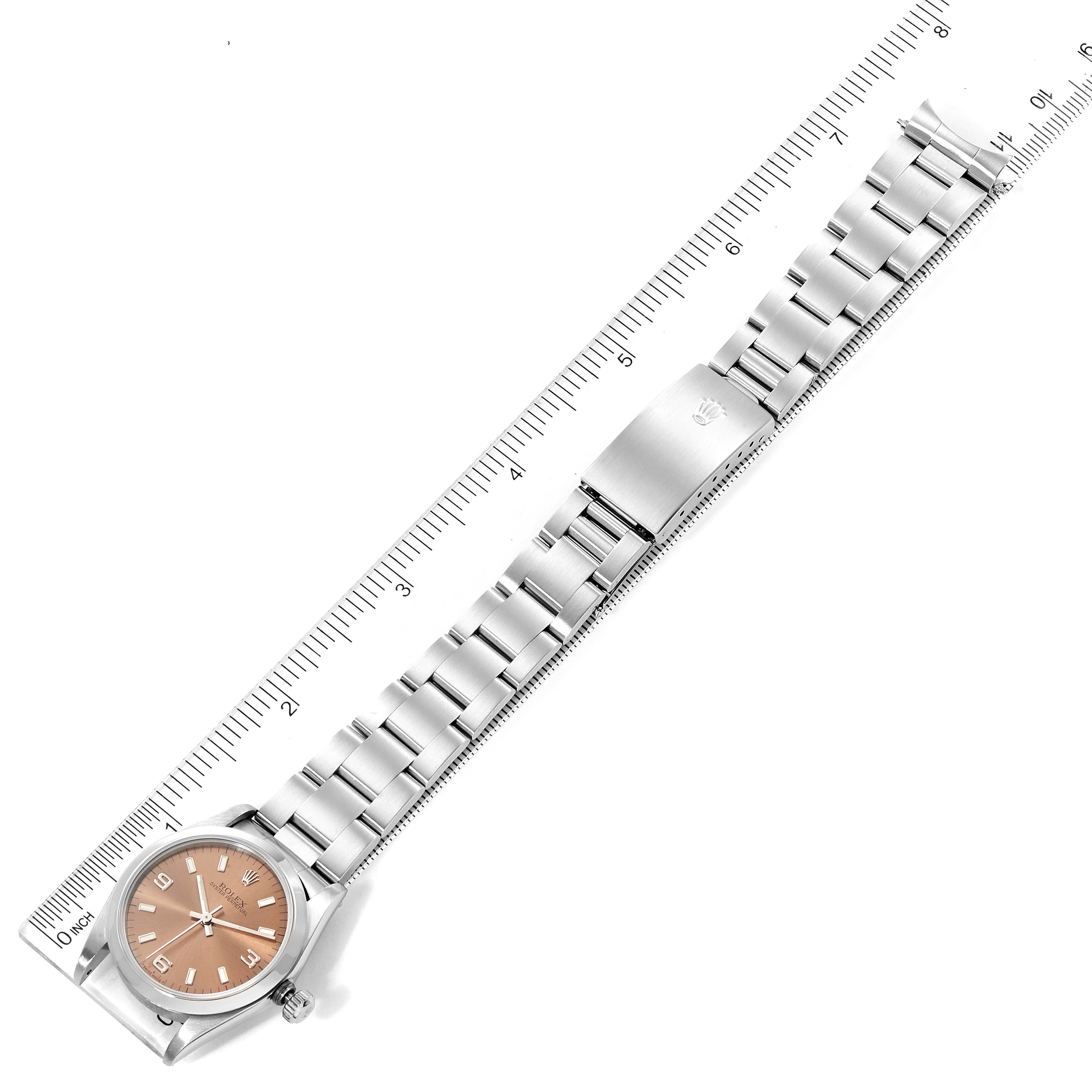 The image shows a Rolex Mid-Size 67480 Women
s Stainless Steel Pink Dial 67480 Women
s Stainless Steel Pink Dial watch laying flat, featuring the face, bracelet, and clasp, with a ruler for scale.