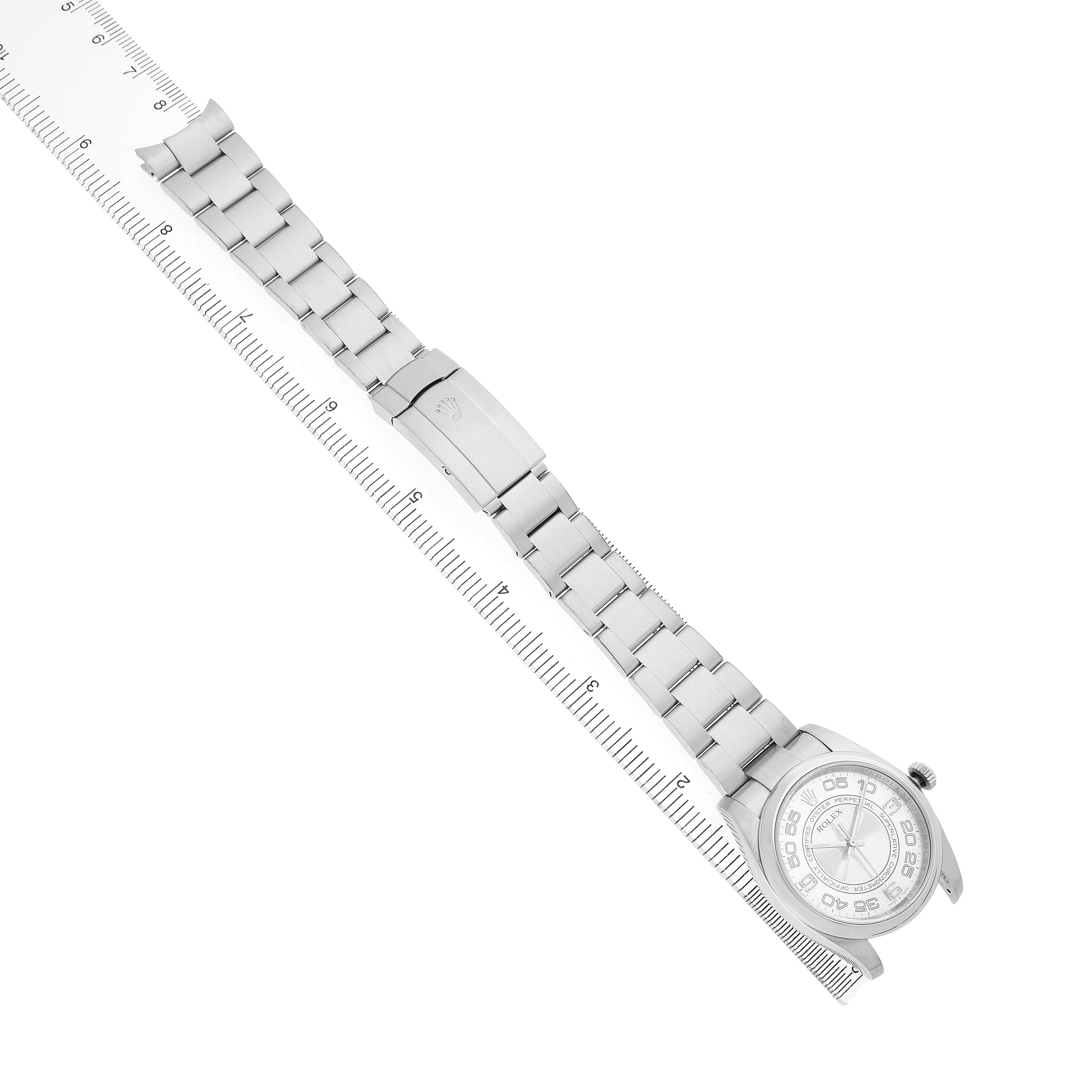 The Rolex Oyster Perpetual 116000 Men's Stainless Steel Silver Dial watch is shown at a diagonal angle, displaying the bracelet and face beside a ruler.