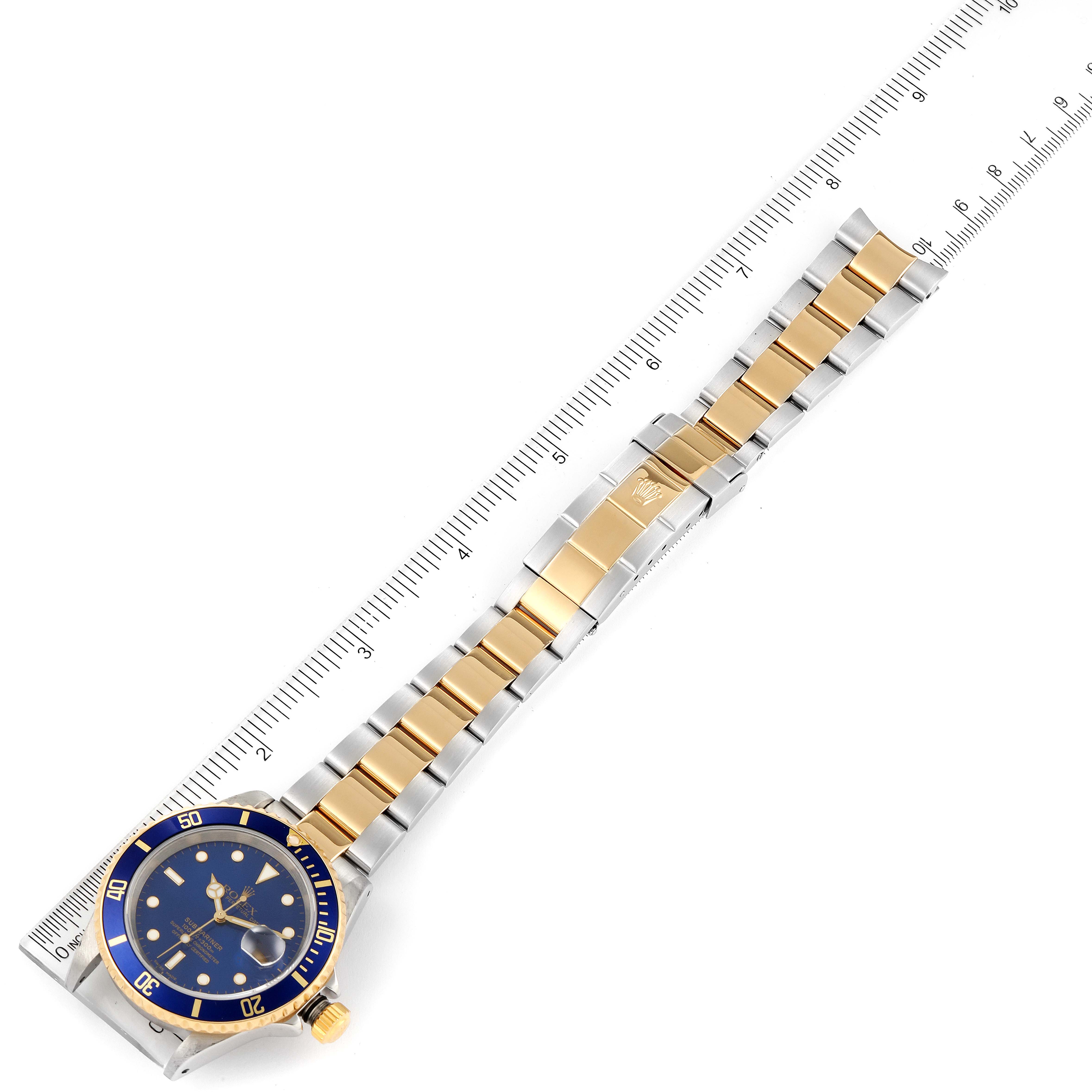 The Rolex Submariner 16613 Men
s Steel and Gold (two tone) Blue Dial 16613 Men
s Steel and Gold (two tone) Blue Dial watch is shown from a top-down angle, showcasing the entire wristband and the face of the watch alongside a ruler.