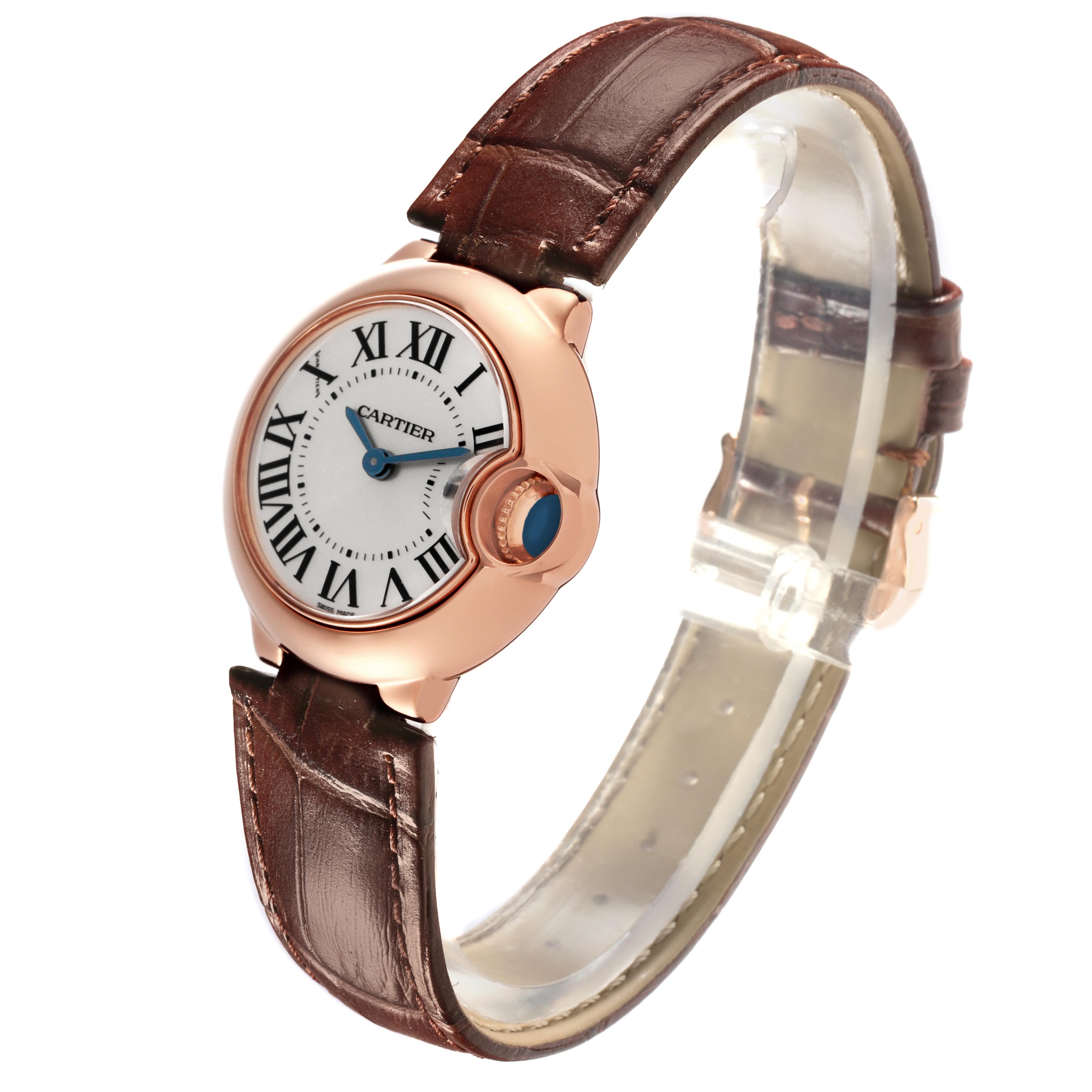 The Ballon Bleu by Cartier is shown from a side angle, highlighting its rose gold case, white dial with Roman numerals, and brown leather strap.