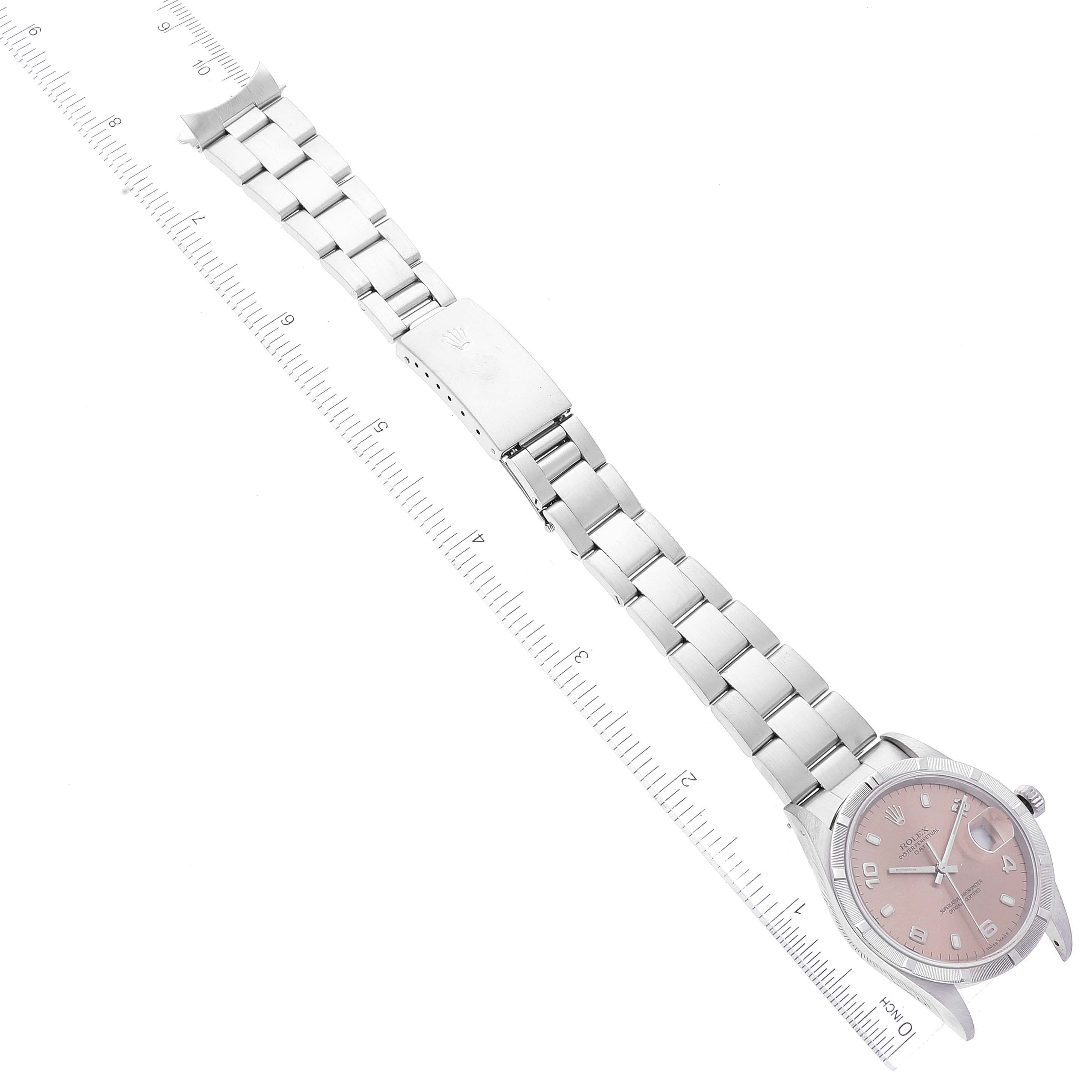 The image shows a Rolex Date 15210 Men
s Stainless Steel Pink Dial 15210 Men
s Stainless Steel Pink Dial model watch from an overhead angle, displaying the face, bracelet, and clasp next to a measurement scale.