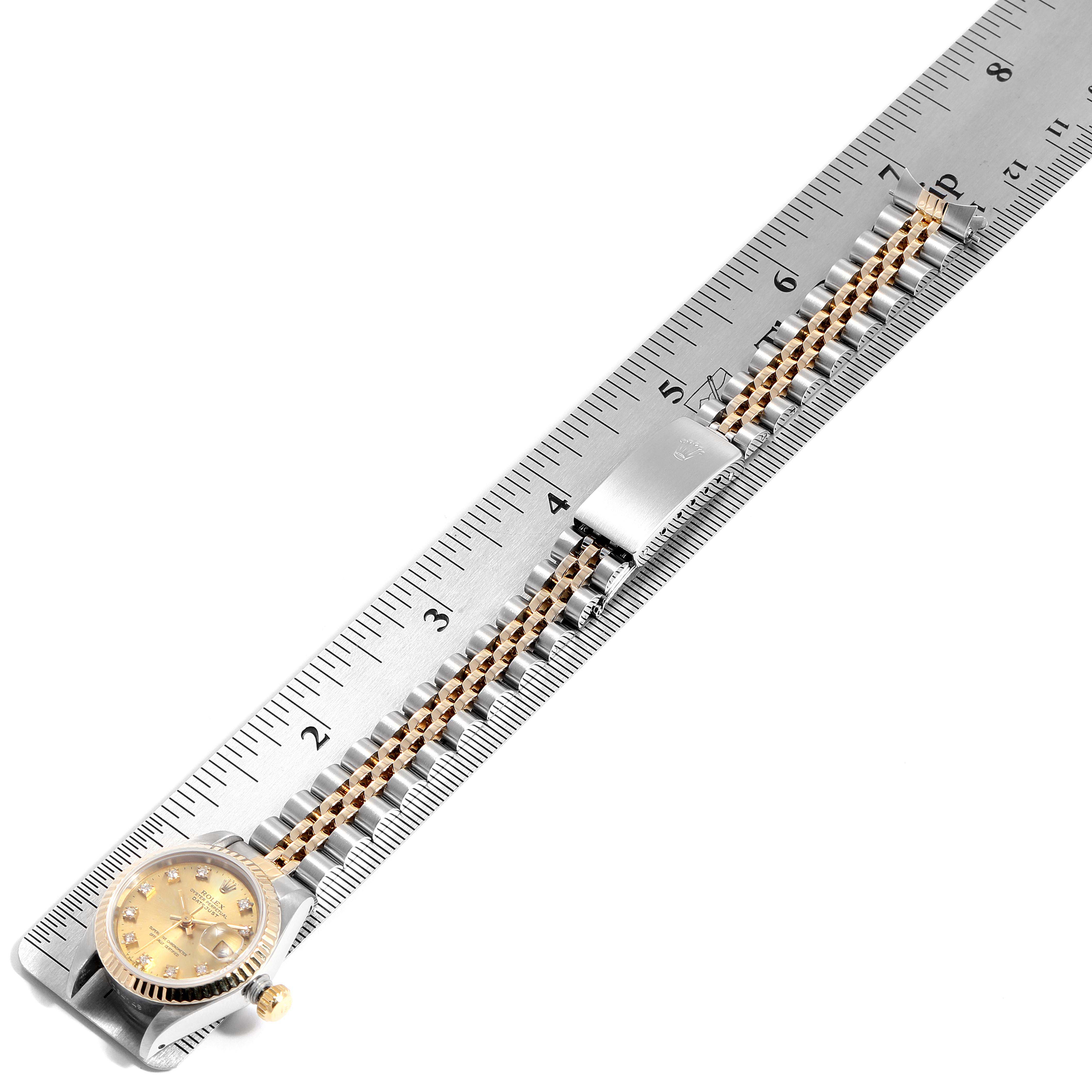 The Rolex Datejust 69173 Women
s Steel and Gold (two tone) Champagne Dial 69173 Women
s Steel and Gold (two tone) Champagne Dial watch is shown at an angled top view along with its bracelet and a ruler for measurement.