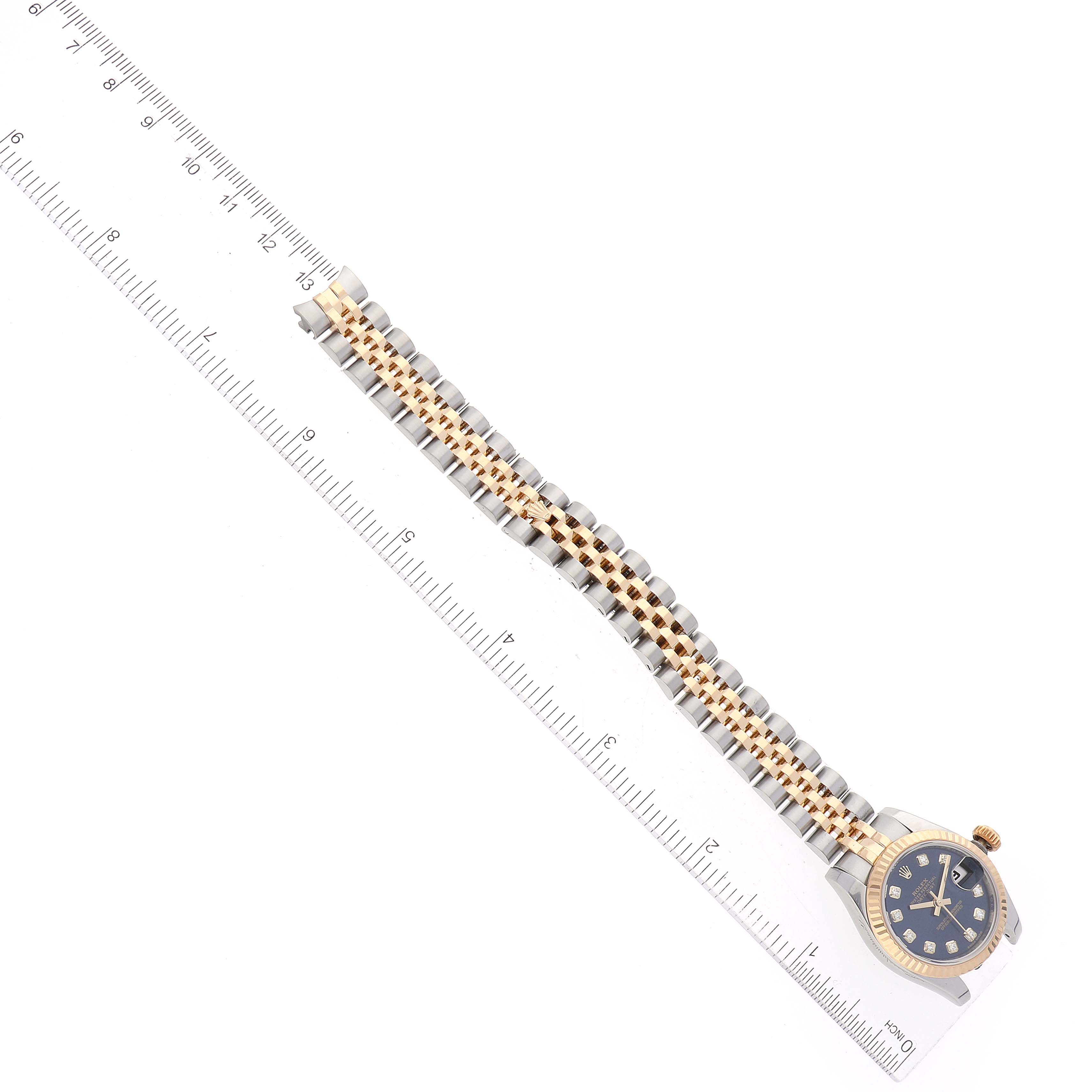 The image shows a Rolex Datejust 179173 Women's Steel and Gold (two tone) Blue Dial 179173 Women's Steel and Gold (two tone) Blue Dial watch with a blue dial and a two-tone bracelet, positioned alongside a ruler for scale.