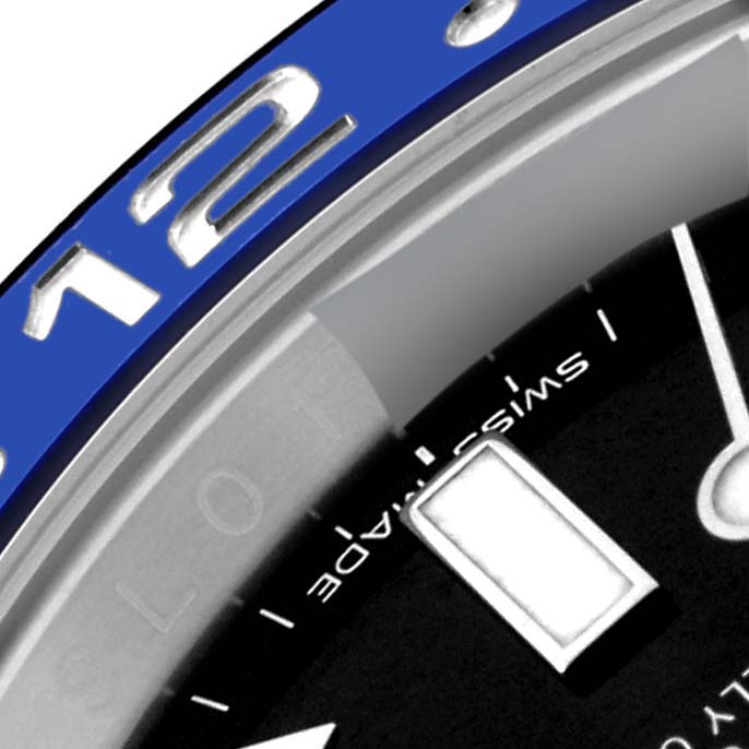 This close-up image of the Rolex GMT-Master 116710 Men
s Stainless Steel Black Dial 116710 Men
s Stainless Steel Black Dial watch shows the bezel with the number twelve, part of the dial, a hand, and a luminescent marker.