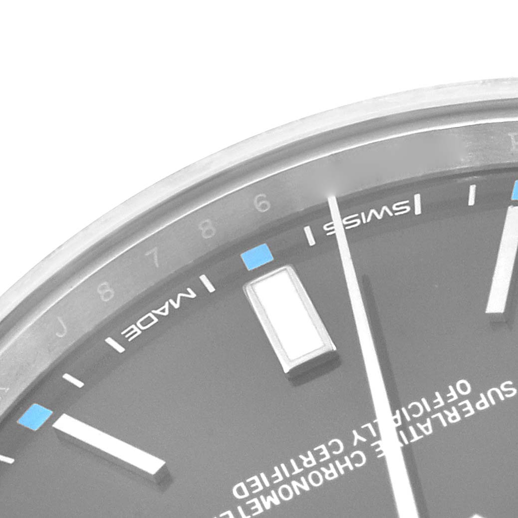 This close-up image shows the dial and part of the bezel of a Rolex Oyster Perpetual 114300 Men's Stainless Steel Grey Dial 114300 Men's Stainless Steel Grey Dial watch, focusing on the hour markers and text.