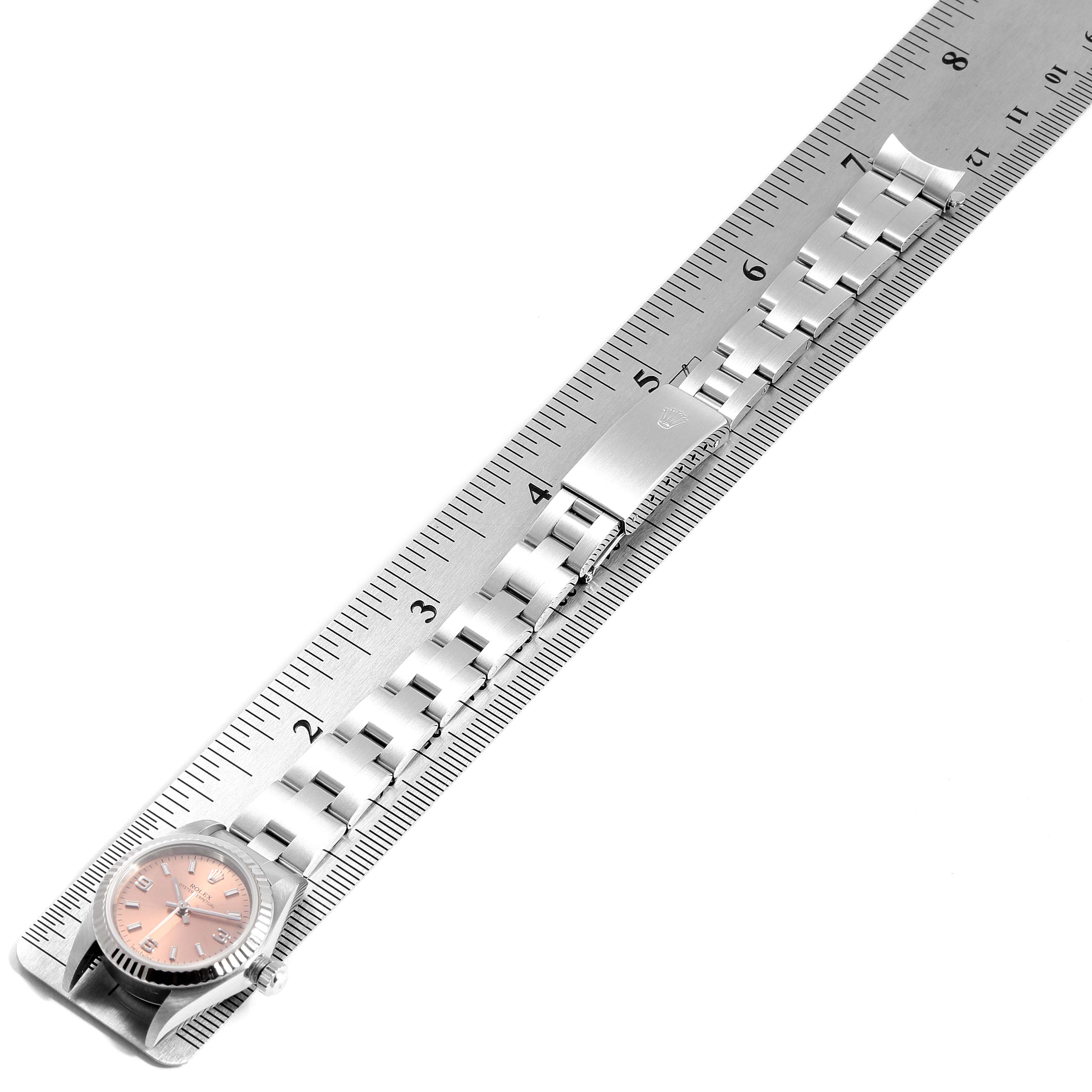 The Rolex Oyster Perpetual 76094 Women's Stainless Steel Pink Dial 76094 Women's Stainless Steel Pink Dial watch is shown in a top-down view, alongside a ruler for scale.