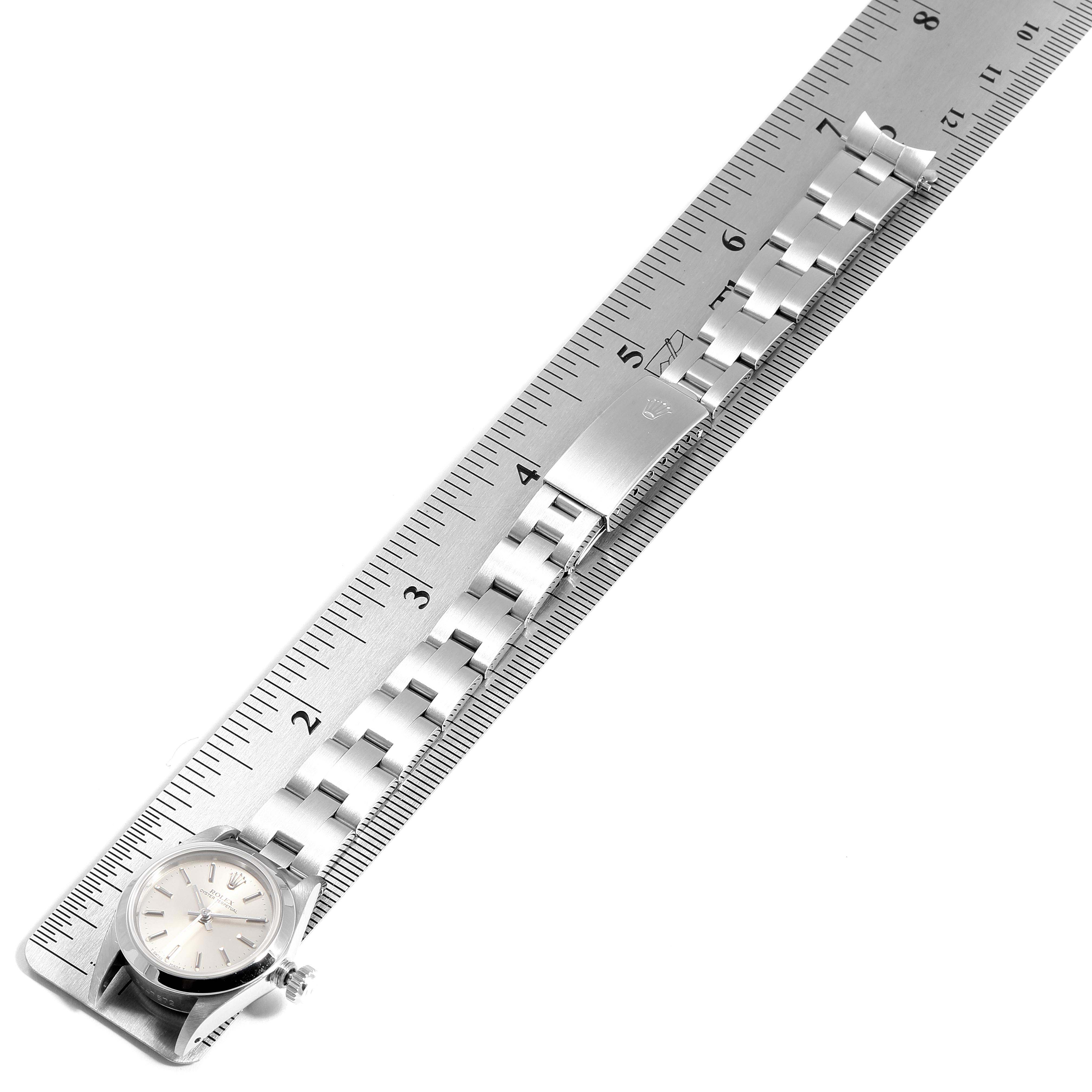 The image shows the dial and metallic bracelet of a Rolex Oyster Perpetual 67180 Women's Stainless Steel Silver Dial 67180 Women's Stainless Steel Silver Dial watch laid against a ruler for measurement.