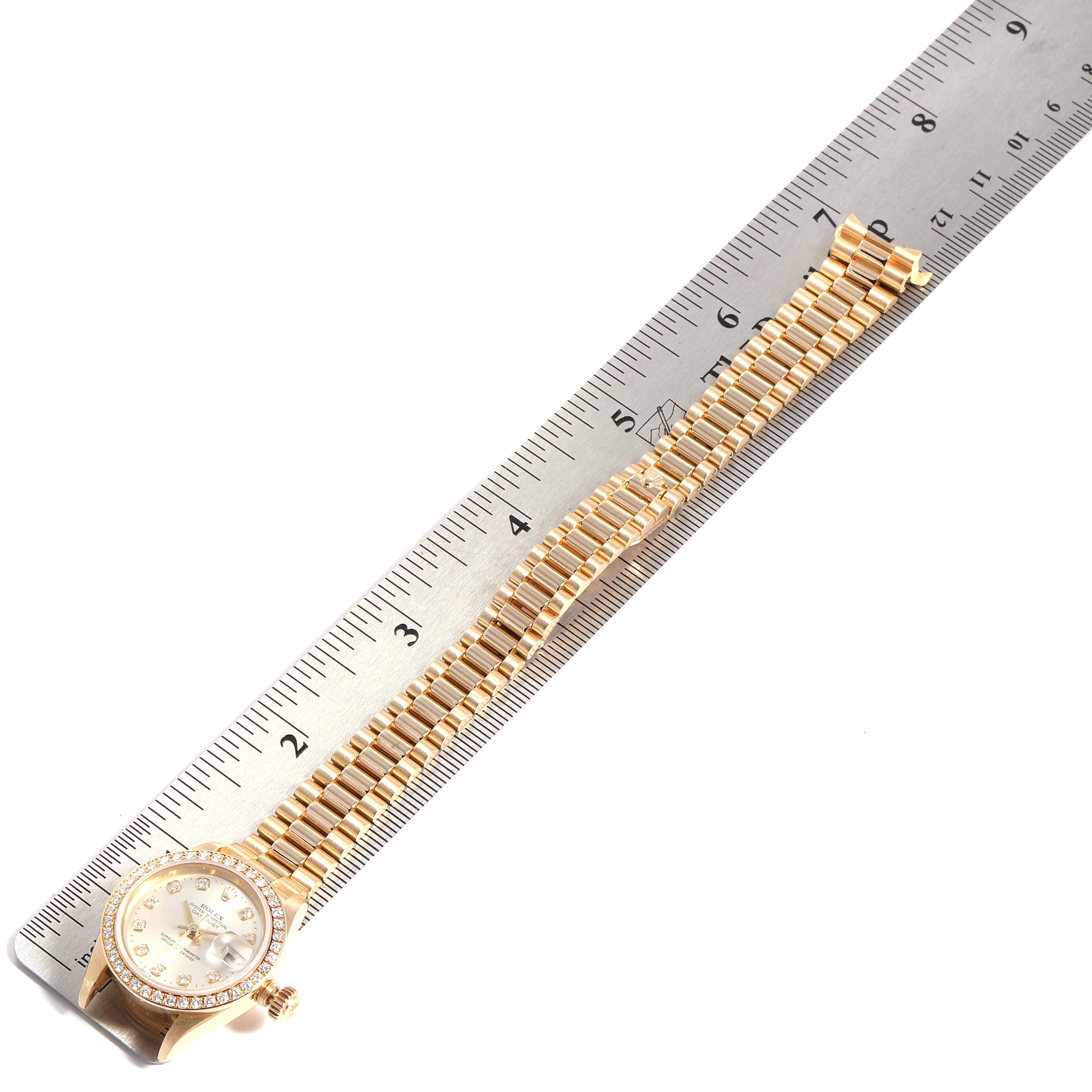 The image shows a Rolex President 79138 Women
s Yellow Gold Silver Dial 79138 Women
s Yellow Gold Silver Dial model watch placed parallel to a ruler, highlighting its band and face.