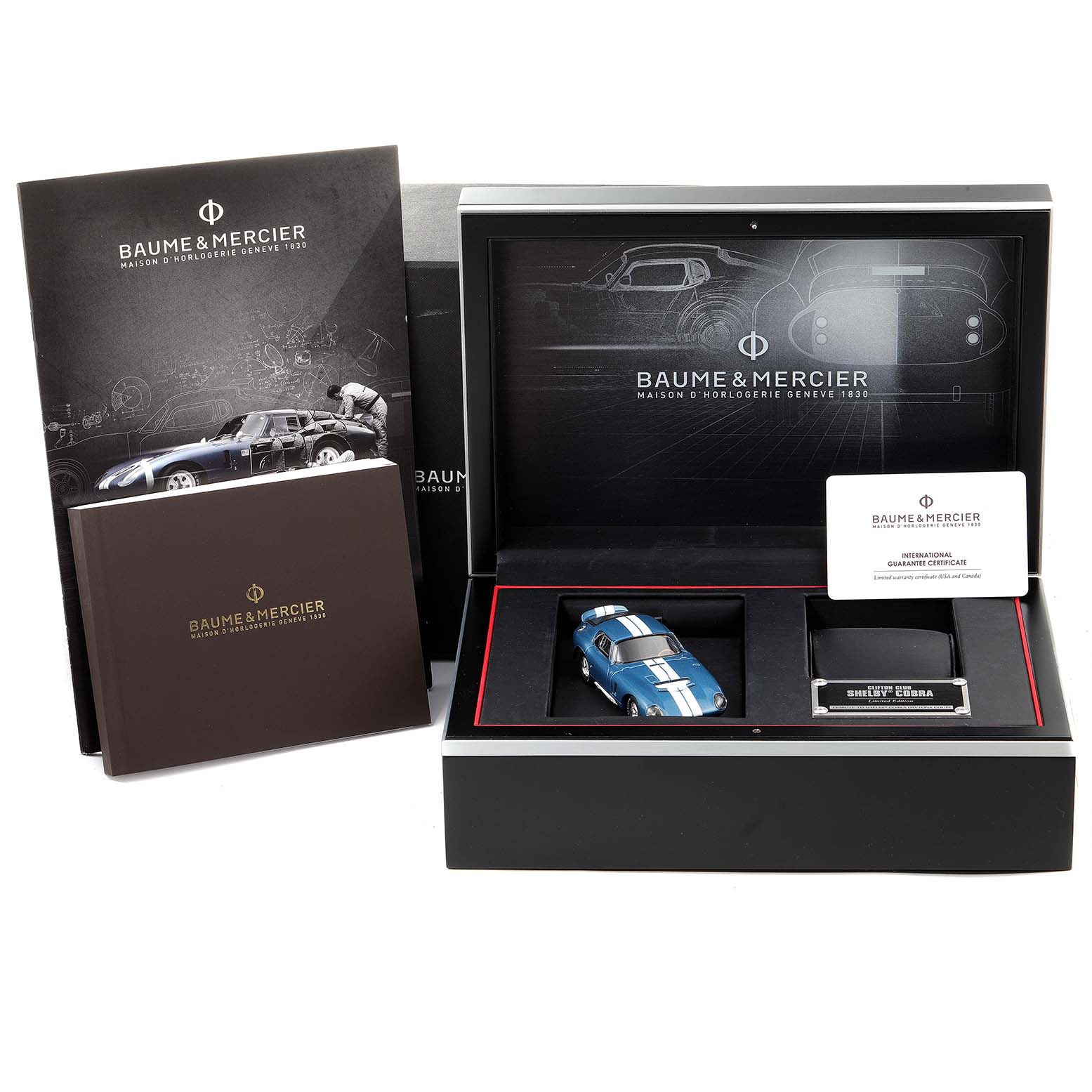 The image shows the box and accessories for the Baume & Mercier Clifton M0A10343 Men's Stainless Steel Blue Dial M0A10343 Men's Stainless Steel Blue Dial model, including a booklet, model car, and guarantee card.