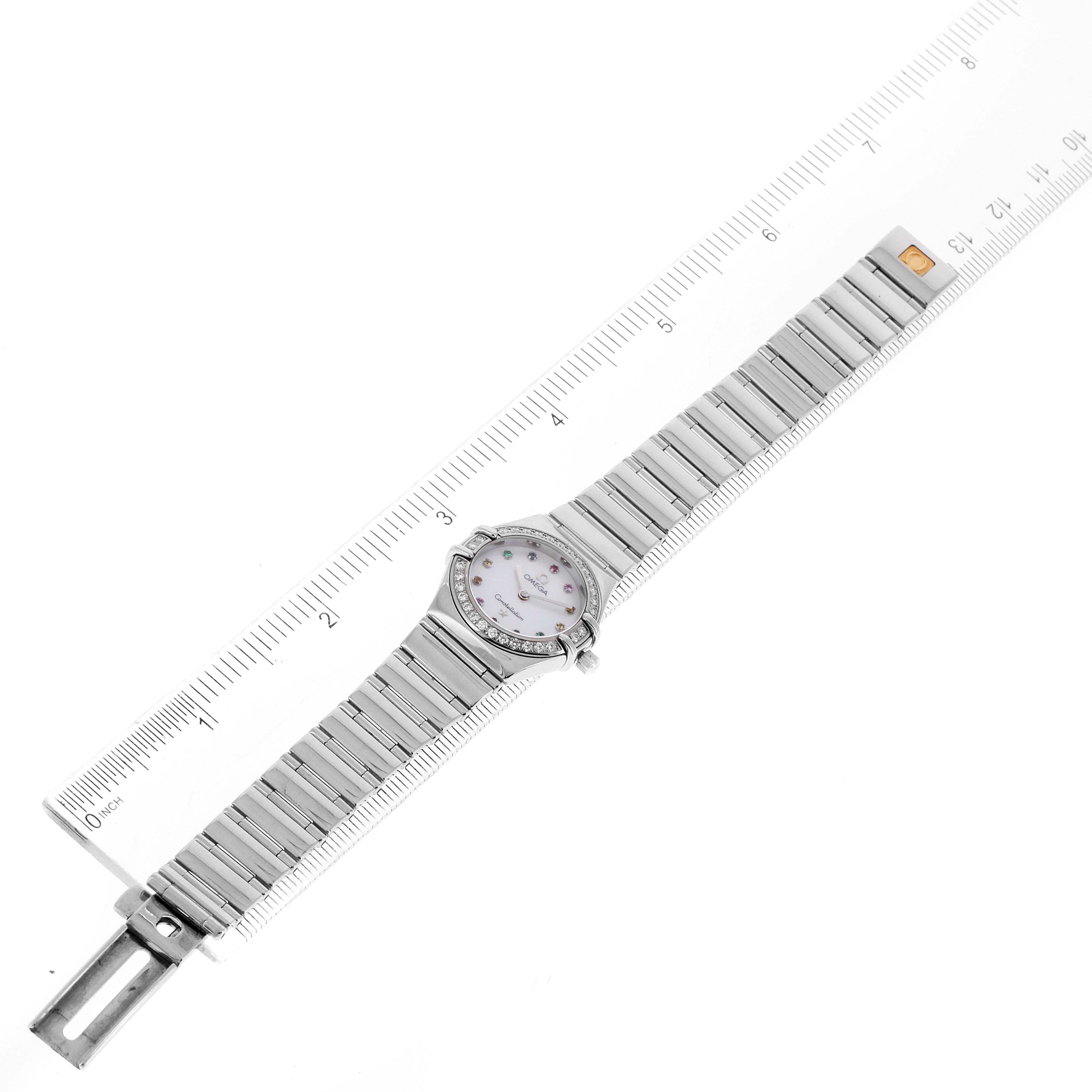 The image shows an overhead view of the Omega 1465.79.00 Women's Stainless Steel Mother of Pearl Dial 1465.79.00 Women's Stainless Steel Mother of Pearl Dial Constellation Iris Rainbow Multi Stone Steel Ladies Watch 1476.79.00 with its full band and face displayed adjacent to a ruler.
