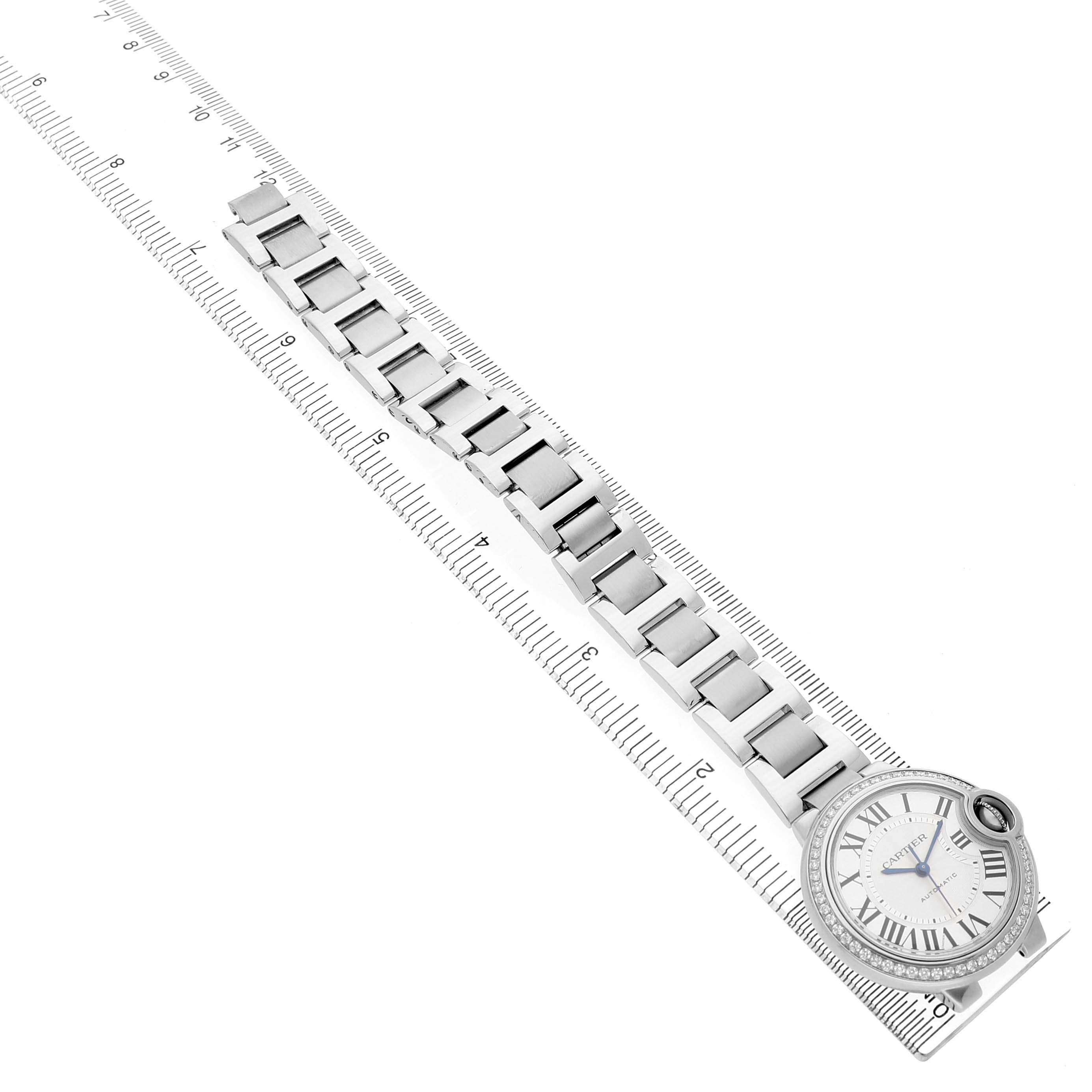 The Cartier Ballon Bleu W4BB0016 Women's Stainless Steel Silver Dial watch is shown from an overhead angle, displaying its face and bracelet aligned on a ruler.