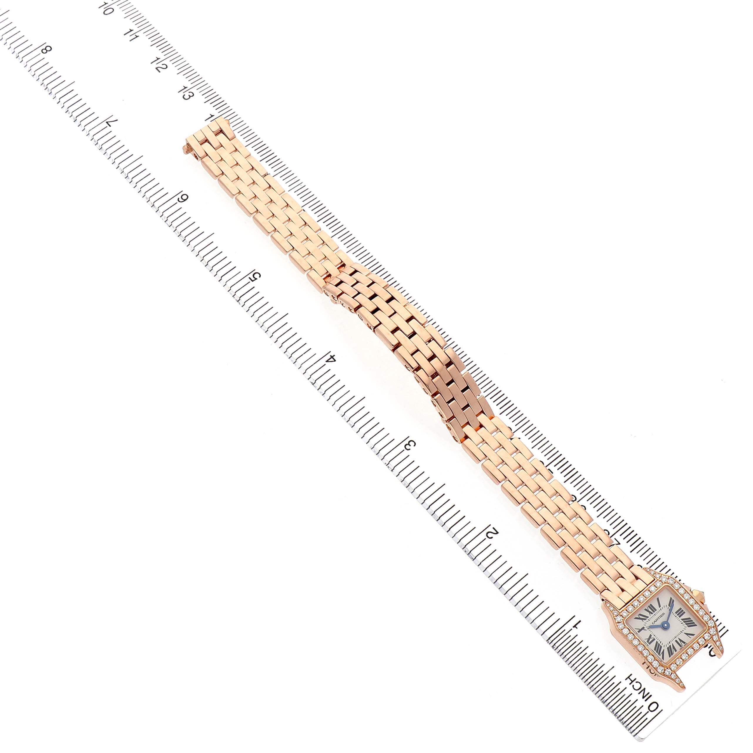 The Cartier Santos WF9011Z8 Women's Rose Gold Silver Dial watch is shown from a top-down angle, highlighting its full gold bracelet and square face next to a ruler.