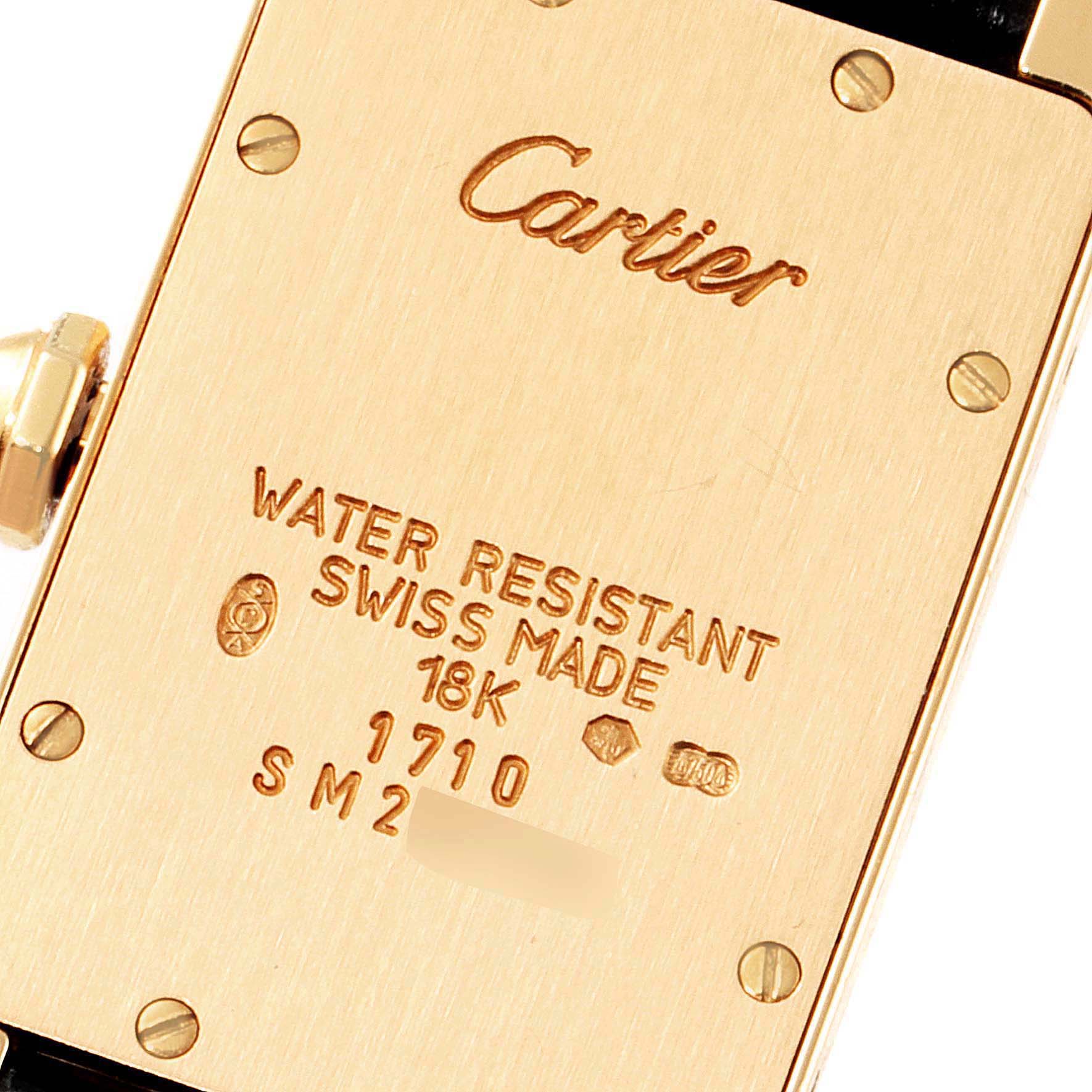 This image shows the gold back case of a Tank Americaine watch by Cartier, featuring inscriptions and screws.
