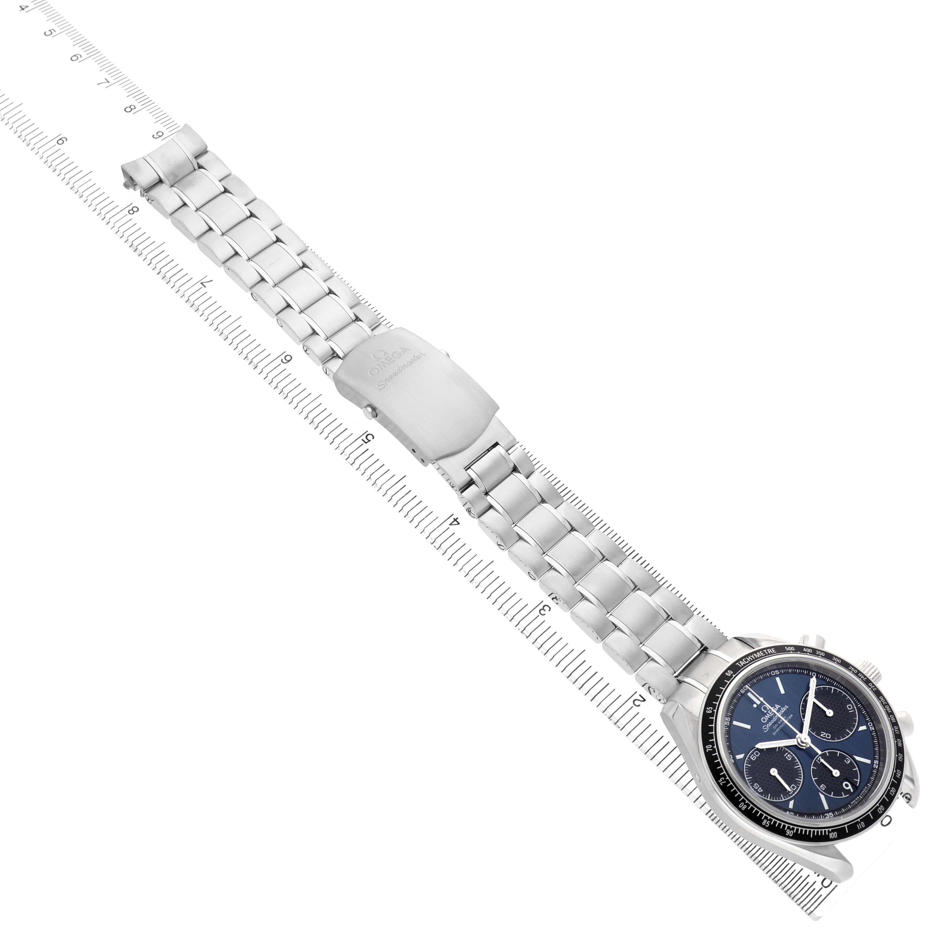 The Omega Speedmaster 326.30.40.50.03.001 Men's Stainless Steel Blue Dial watch is shown diagonally from the top, displaying its face, bracelet, and clasp on a ruler backdrop.