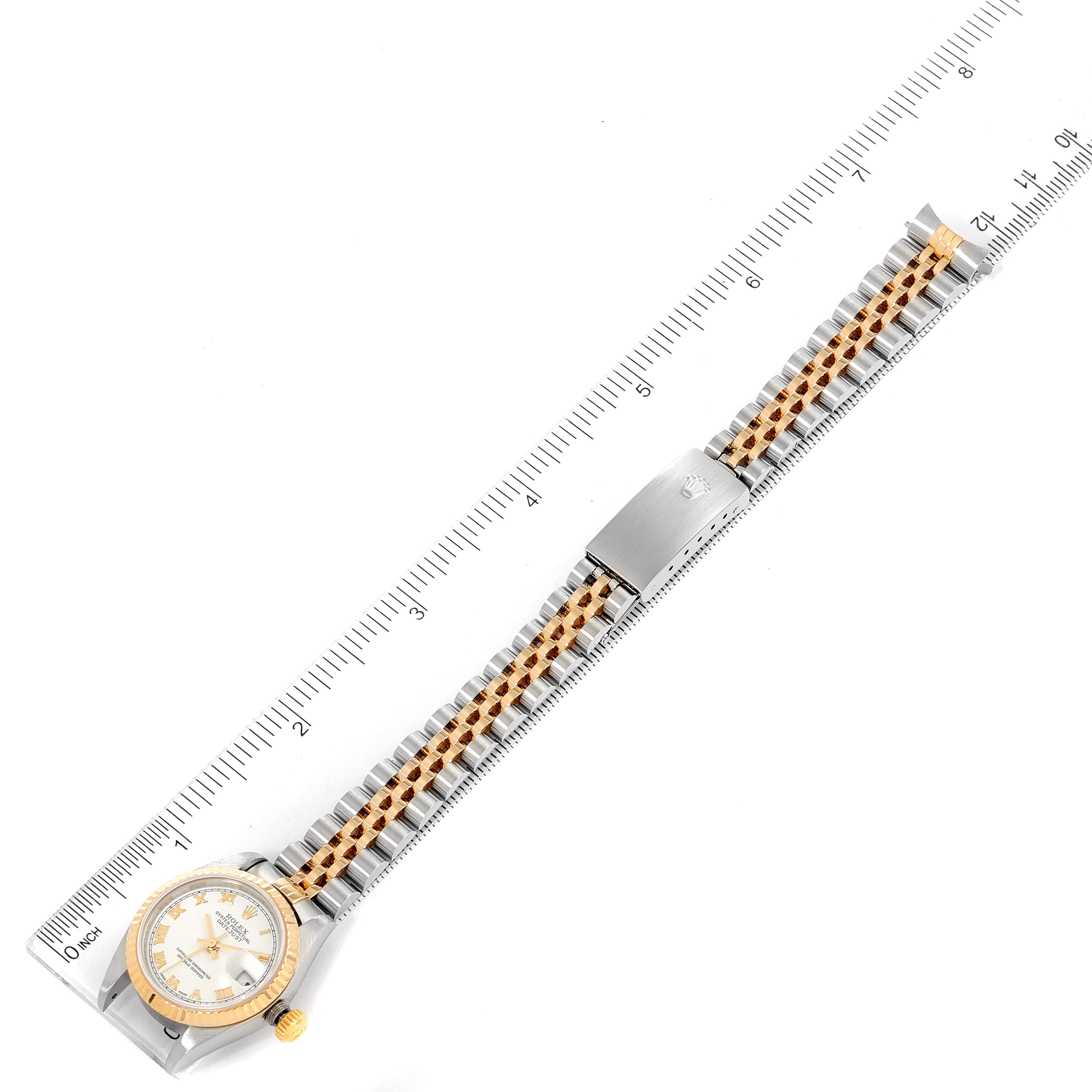 This image shows the Rolex Datejust 79173 Women
s Steel and Gold (two tone) White Dial 79173 Women
s Steel and Gold (two tone) White Dial watch from a top-down angle, displaying the bracelet, clasp, face, and bezel against a ruler backdrop.