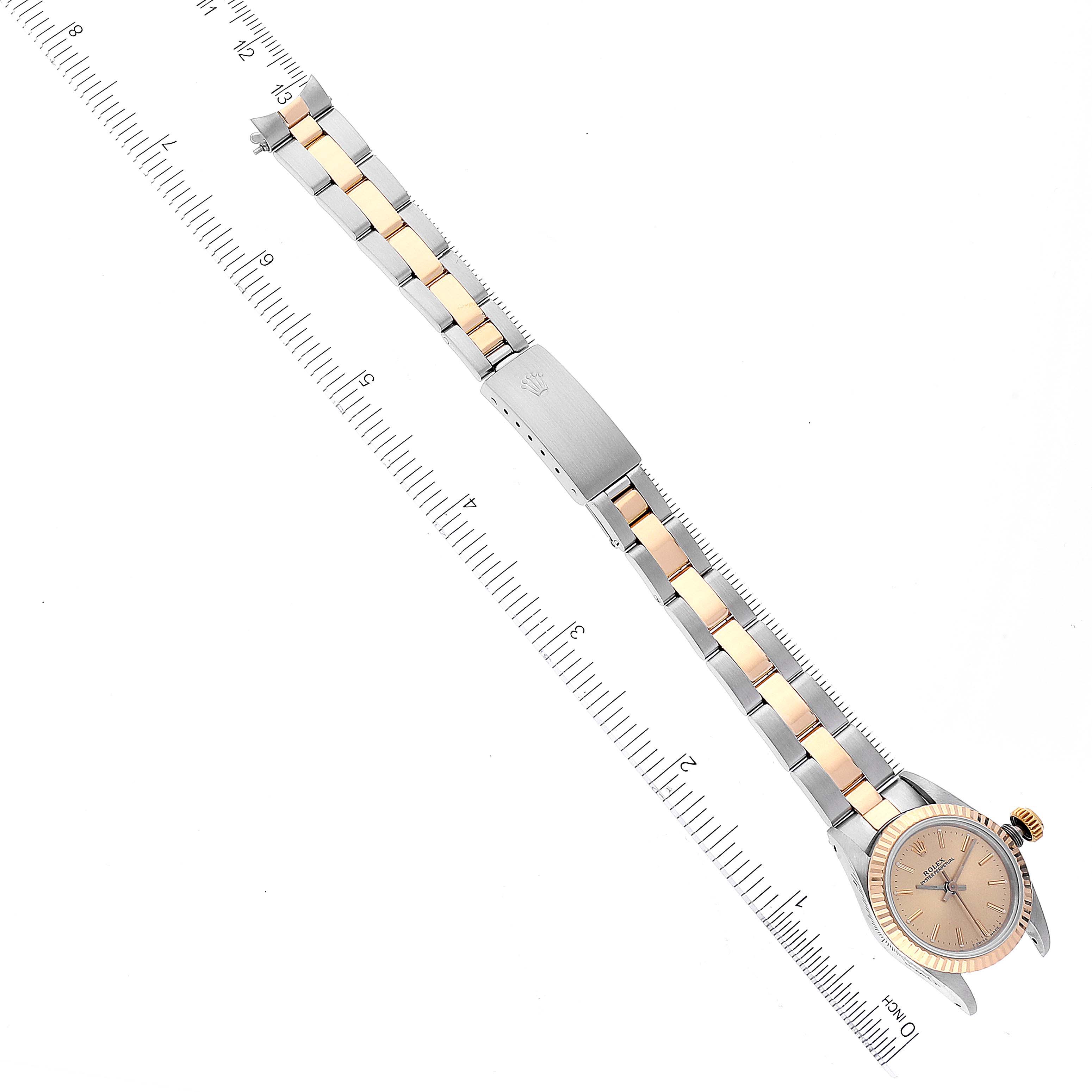 The image shows an overhead view of a Rolex Oyster Perpetual 67193 Women
s Steel and Gold (two tone) Champagne Dial 67193 Women
s Steel and Gold (two tone) Champagne Dial watch, displaying its full band and face against a ruler for scale.