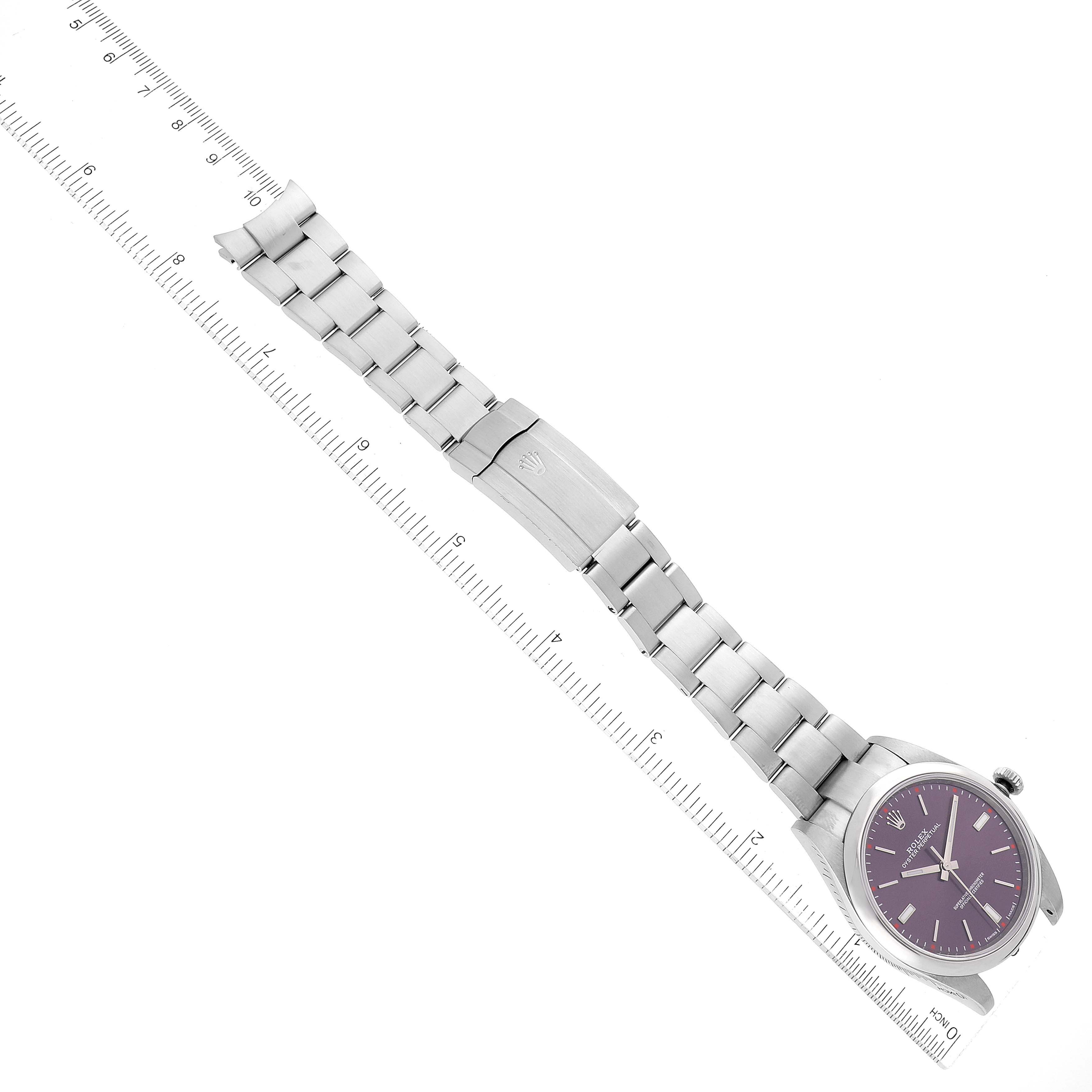 This image shows a top-down view of a Rolex Oyster Perpetual 114300 Men's Stainless Steel Burgundy Dial 114300 Men's Stainless Steel Burgundy Dial watch, including its dial, bracelet, and clasp, next to a ruler.