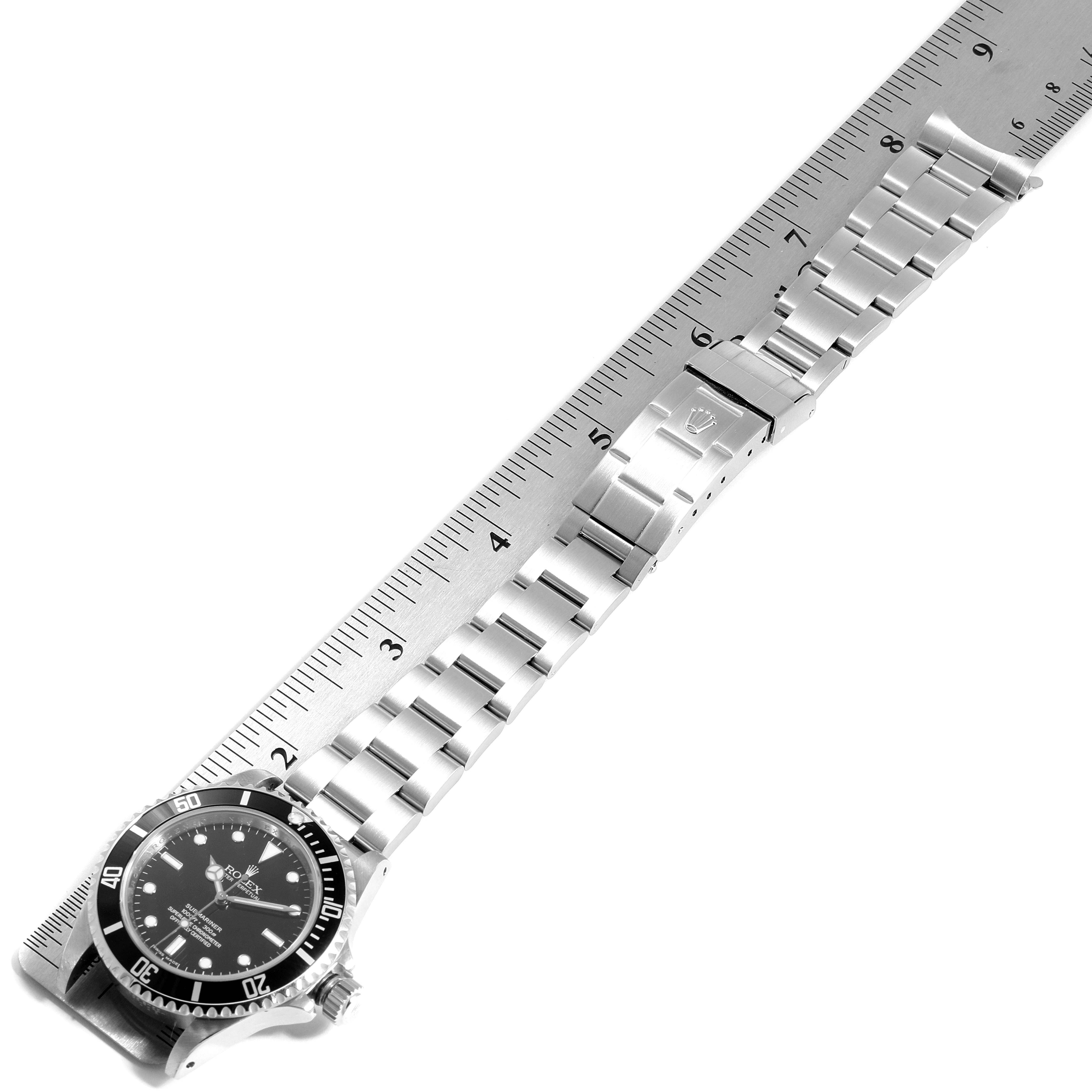 This image shows a Rolex Submariner 14060M Men
s Stainless Steel Black Dial 14060M Men
s Stainless Steel Black Dial watch laid flat against a ruler, displaying both the watch face and the metal bracelet.
