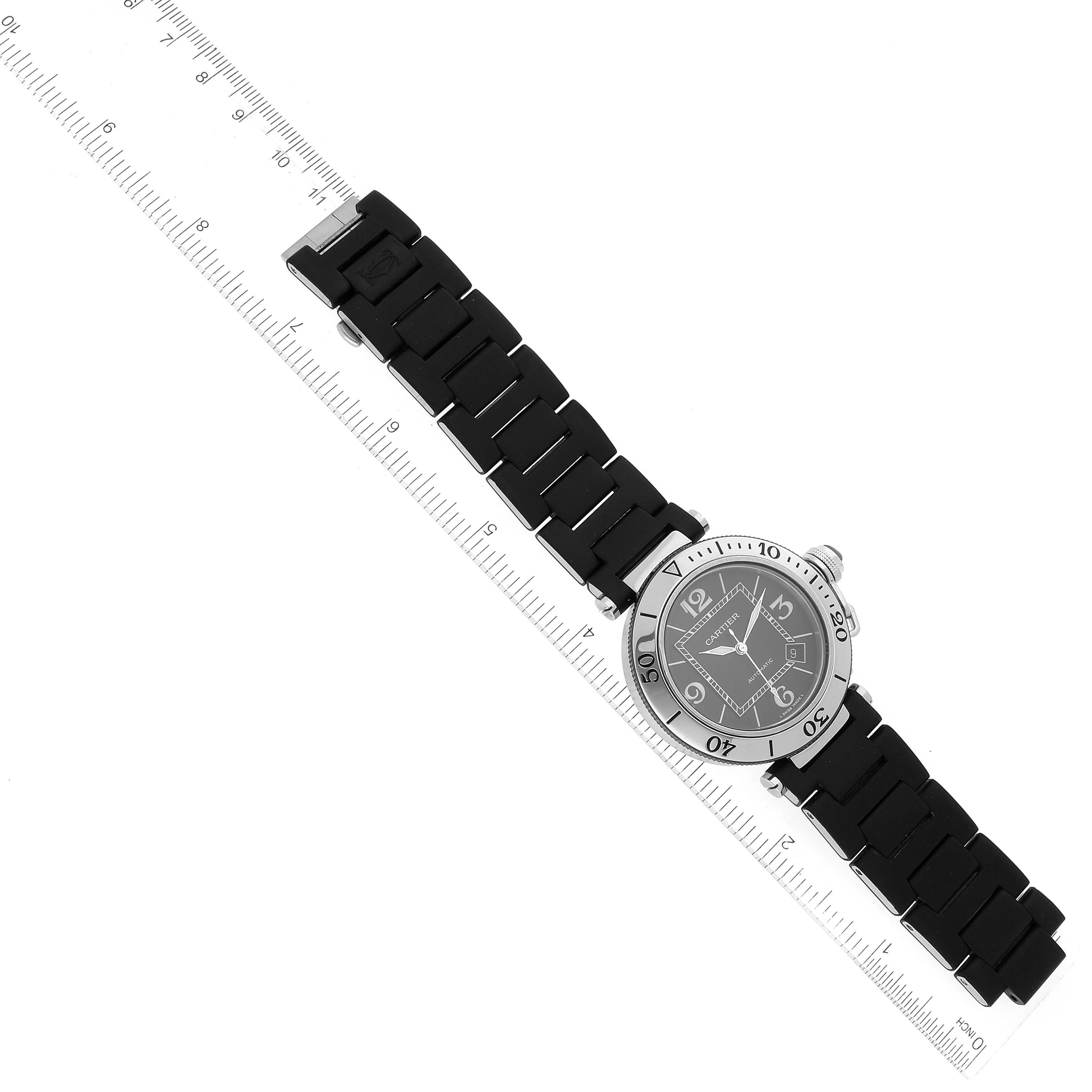 The Cartier Pasha W31077U2 Men
s Stainless Steel Black Dial W31077U2 Men
s Stainless Steel Black Dial watch is shown at a diagonal angle with a ruler beside it, displaying the watch face and the full strap.