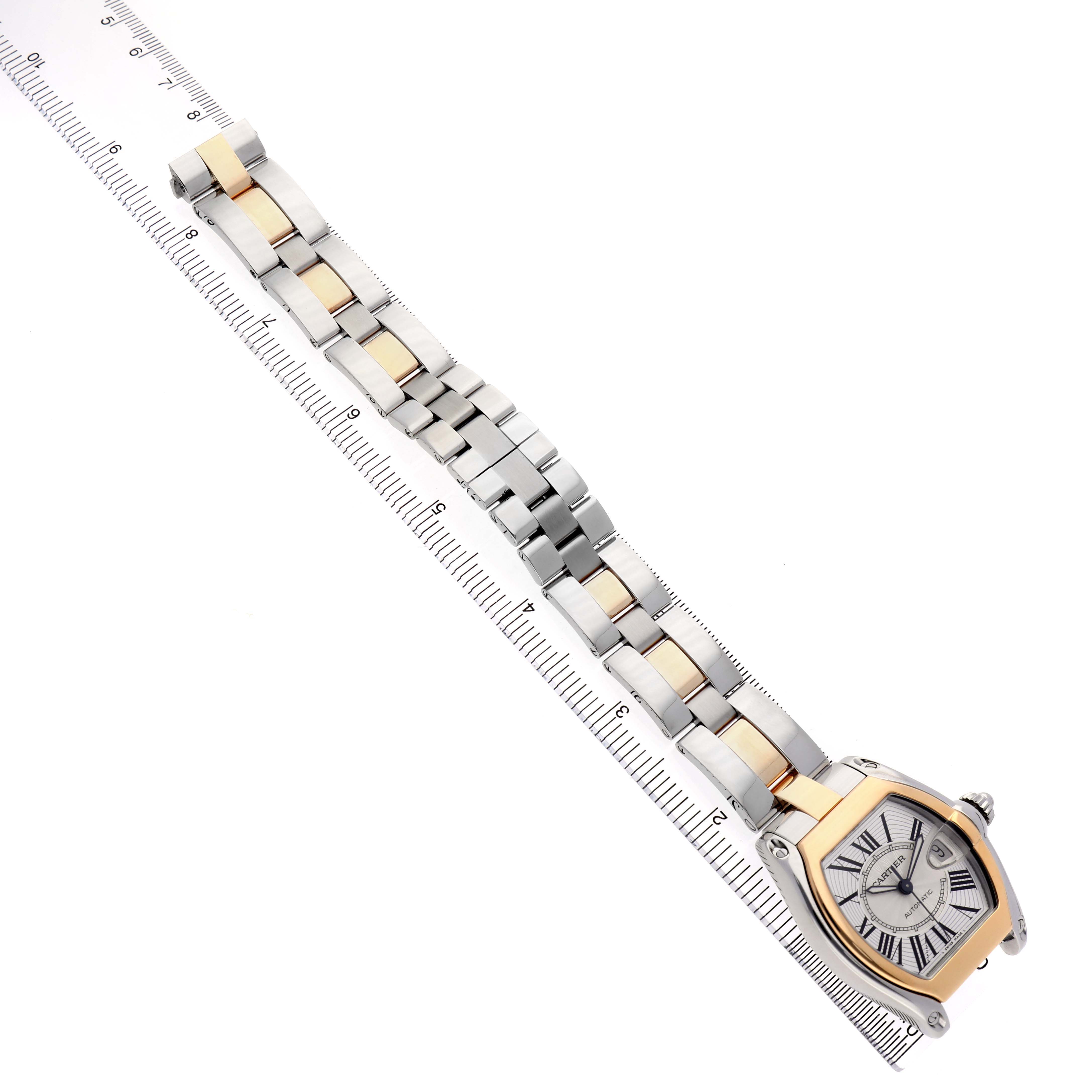 The Cartier Roadster W62031Y4 Men's Steel and Gold (two tone) Silver Dial watch is viewed from above, displaying the face, bezel, bracelet, and clasp alongside a ruler for scale.
