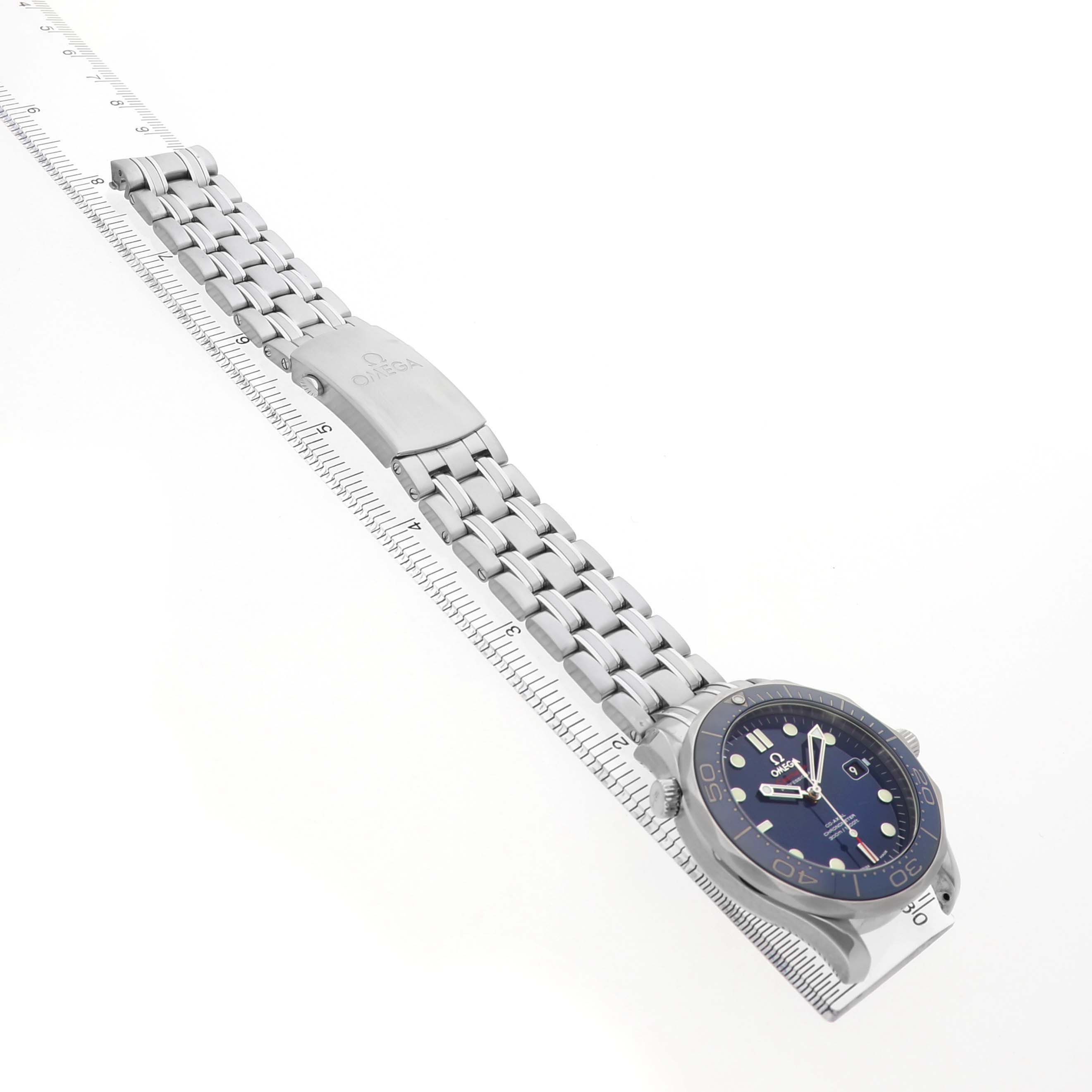 The Omega Seamaster 212.30.41.20.03.001 Men's Stainless Steel Blue Dial watch is shown at an oblique angle, highlighting the blue dial, bezel, and metal bracelet with a clasp on a ruler.