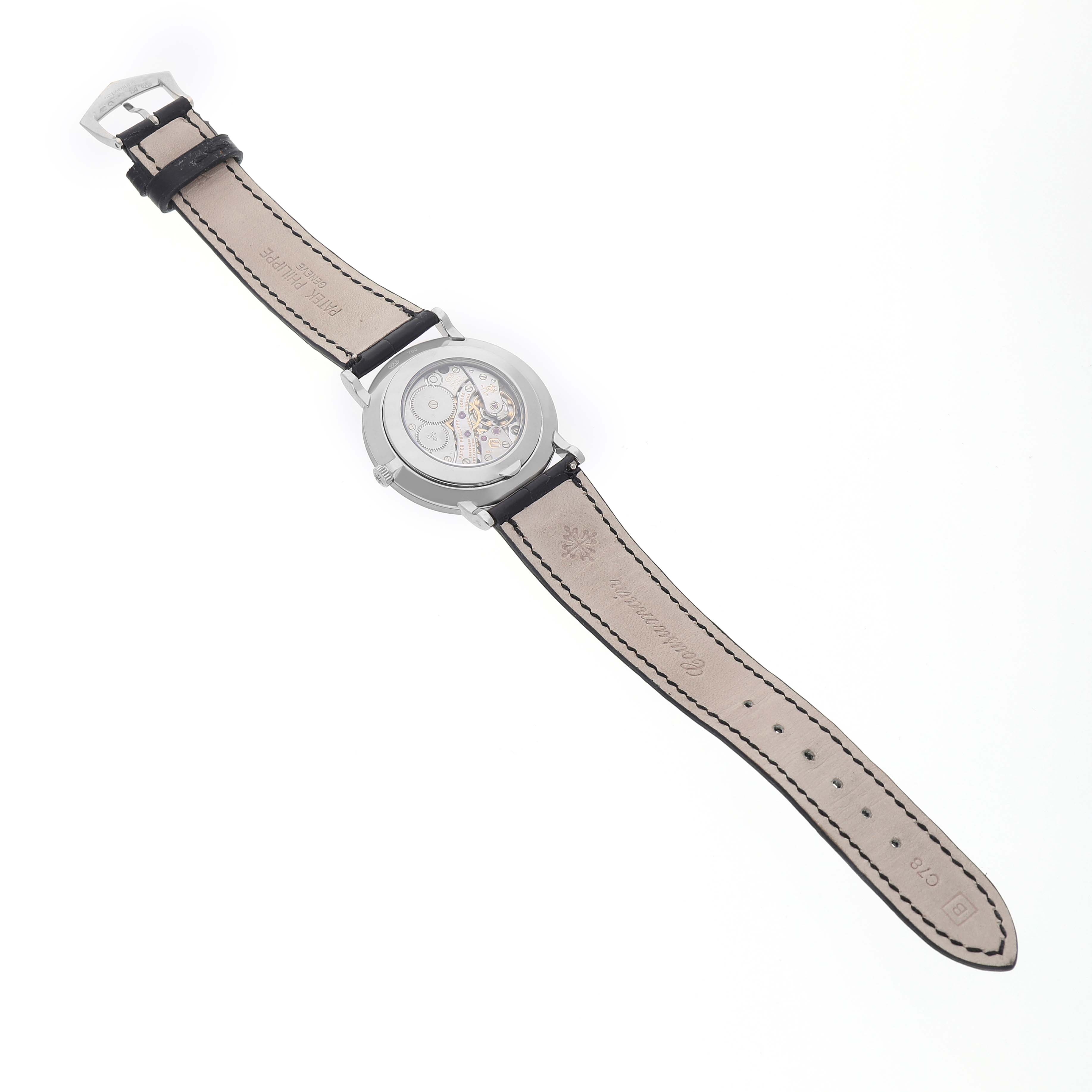 The Patek Philippe Calatrava 5116 Men's White Gold White Dial watch is shown from the back, displaying its movement and leather strap with visible stitching.