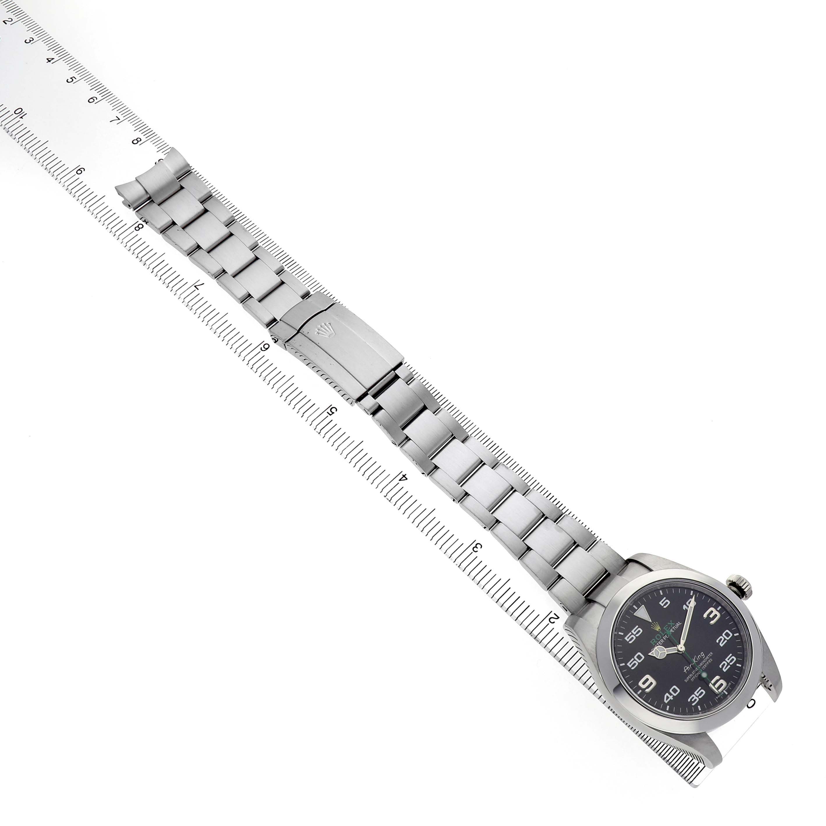 The Rolex Air-King 116900 Men's Stainless Steel Black Dial watch is displayed at an angle, showing the face, bracelet, and clasp aligned along a ruler for measurement.