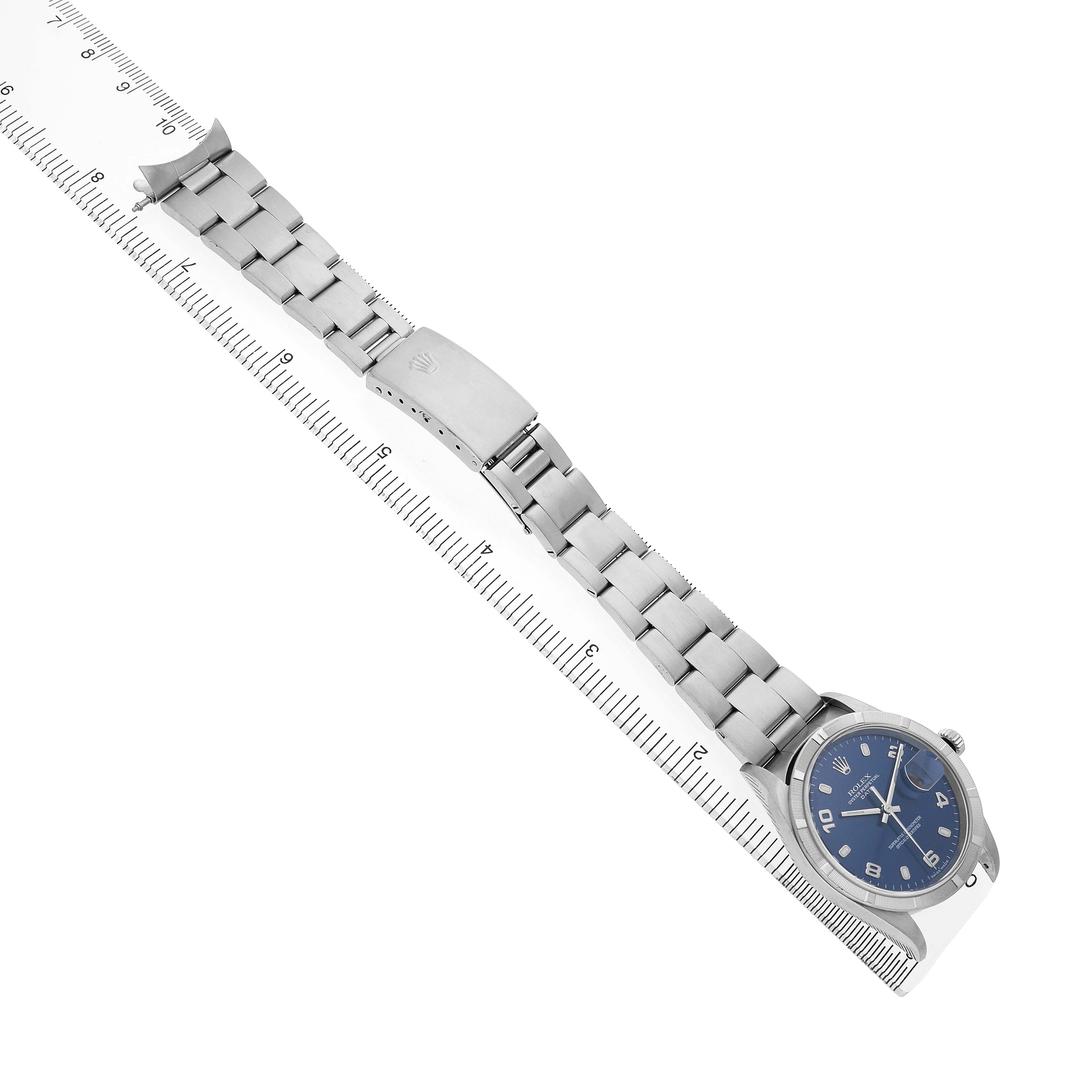 The Rolex Date 15210 Men's Stainless Steel Blue Dial watch is shown from an overhead angle, displaying its full bracelet and clasp alongside a ruler for scale.