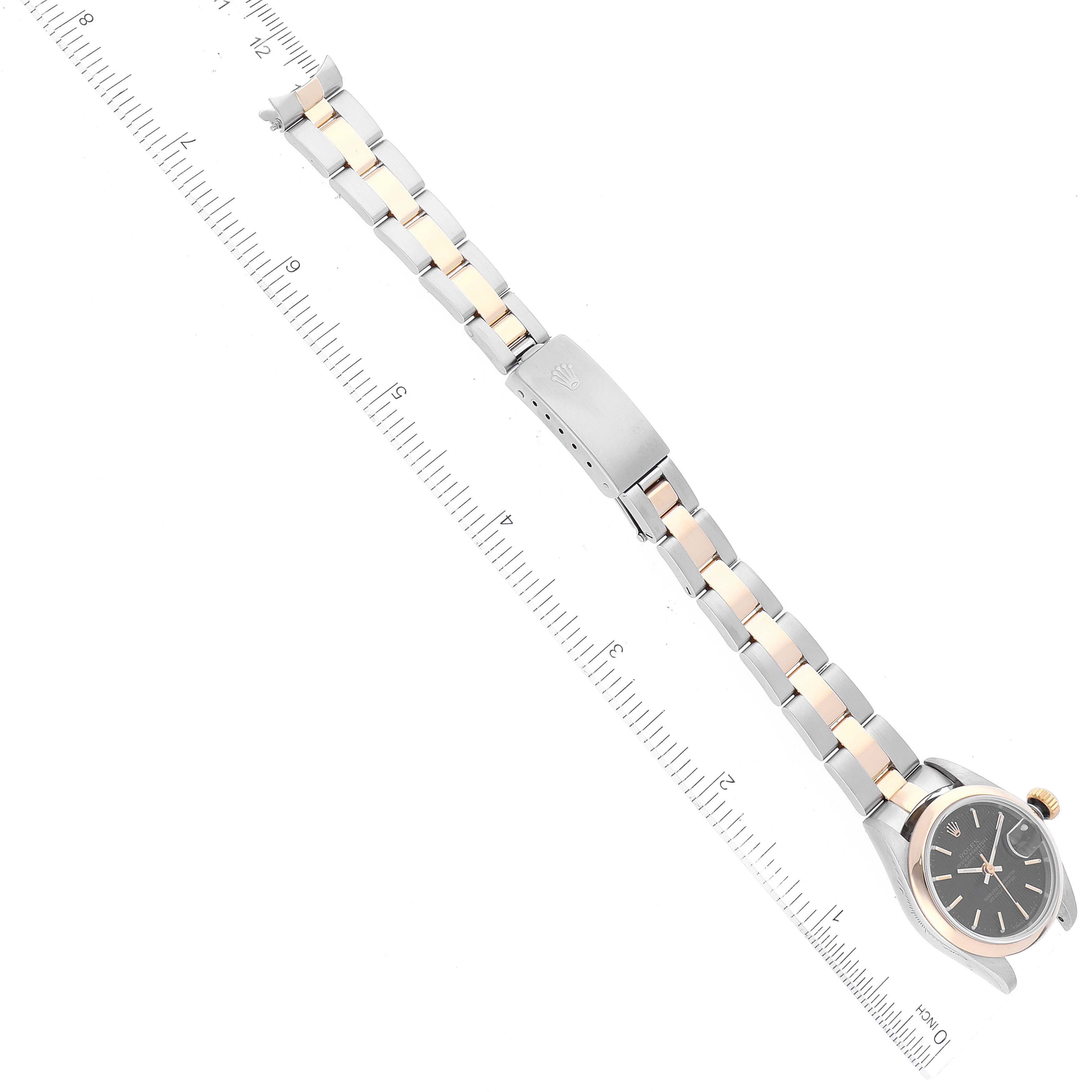 The Rolex Datejust 69163 Women's Steel and Gold (two tone) Black Dial 69163 Women's Steel and Gold (two tone) Black Dial watch is shown from an aerial view, showcasing the face, bracelet, and clasp against a ruler for scale.