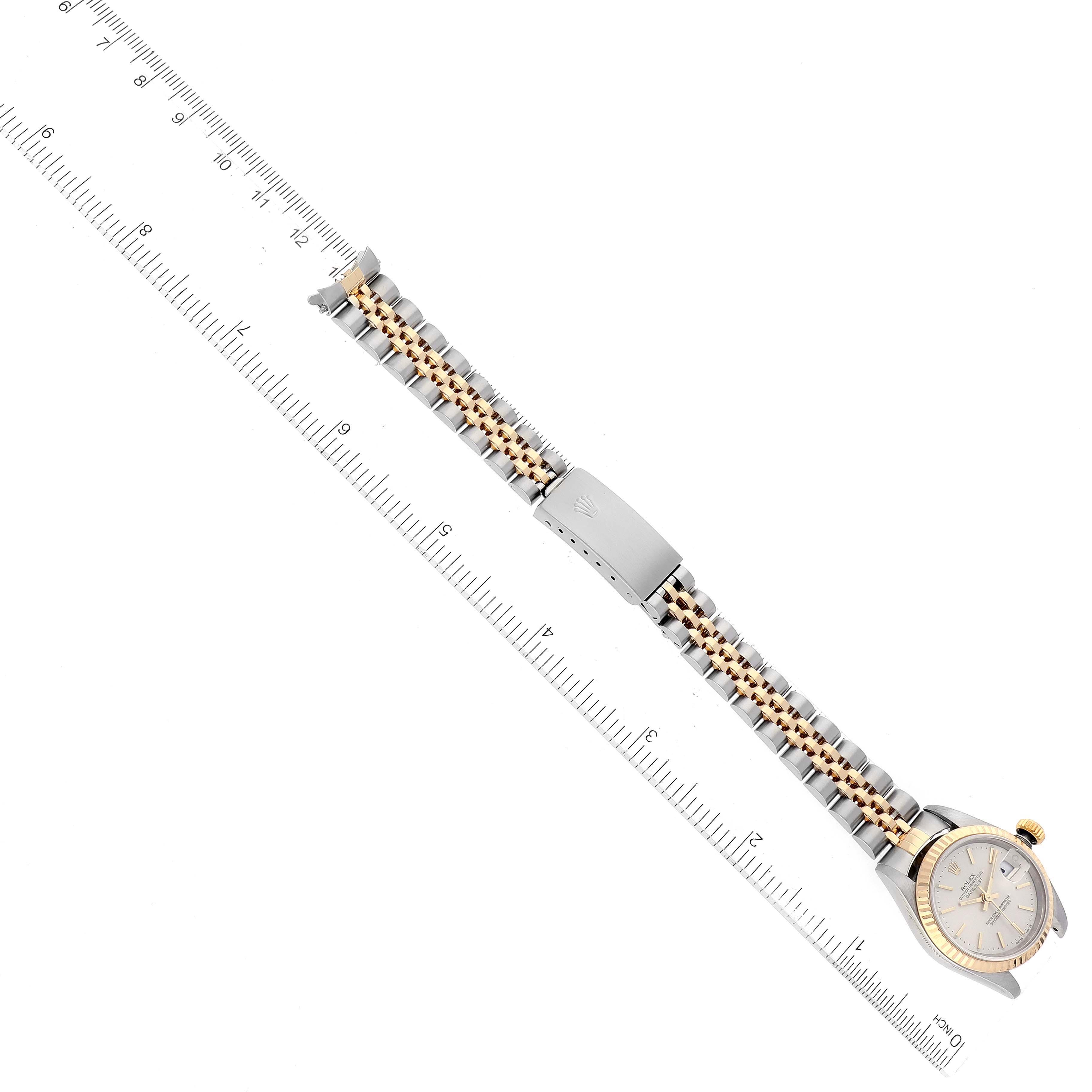 This image shows a Rolex Datejust 79173 Women's Steel and Gold (two tone) Silver Dial 79173 Women's Steel and Gold (two tone) Silver Dial watch laid flat alongside a ruler, highlighting its bracelet and clasp.