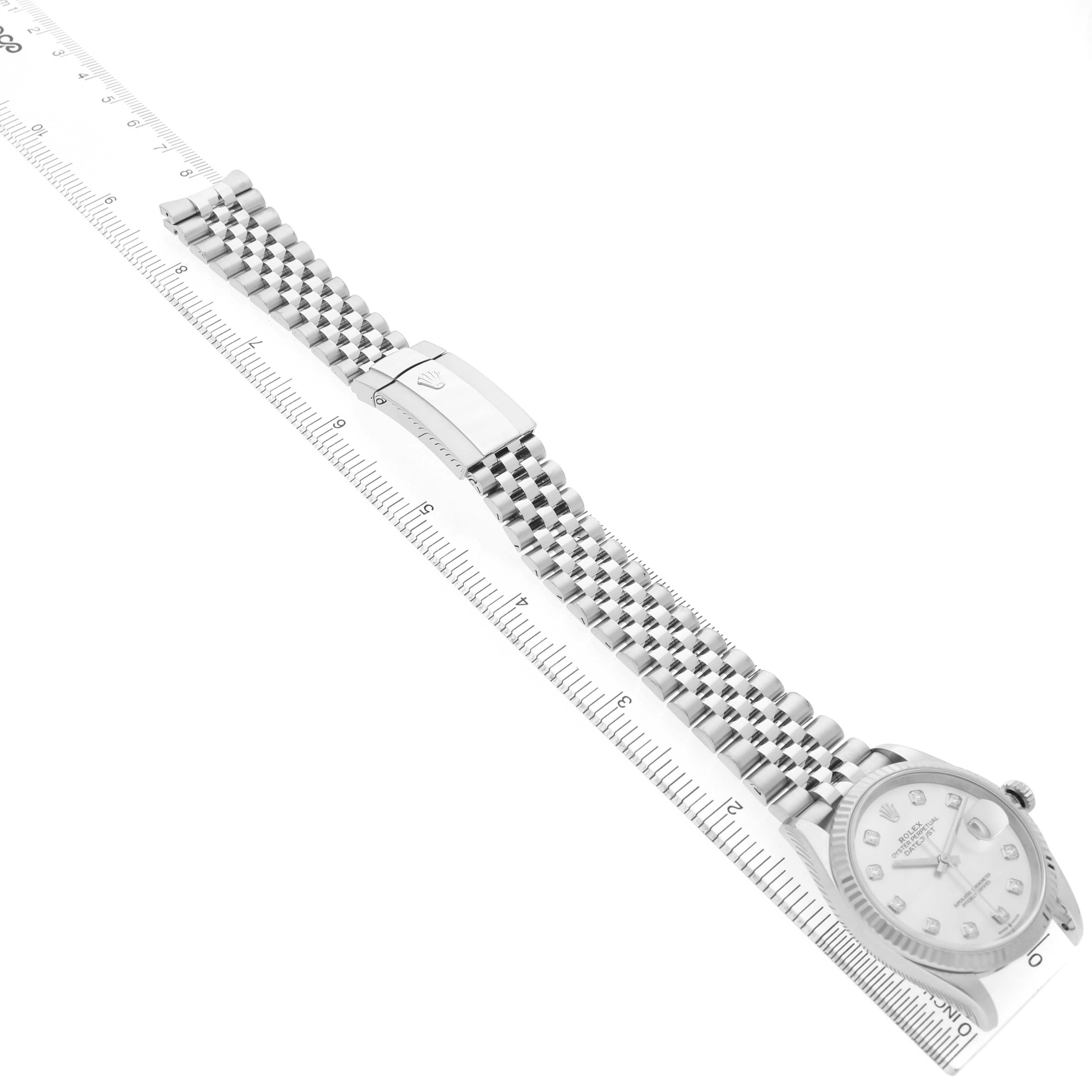 The Rolex Datejust 126234 Men's Stainless Steel Mother of Pearl Dial watch is laid flat, showing its face, bracelet, and clasp at an angle alongside a ruler.