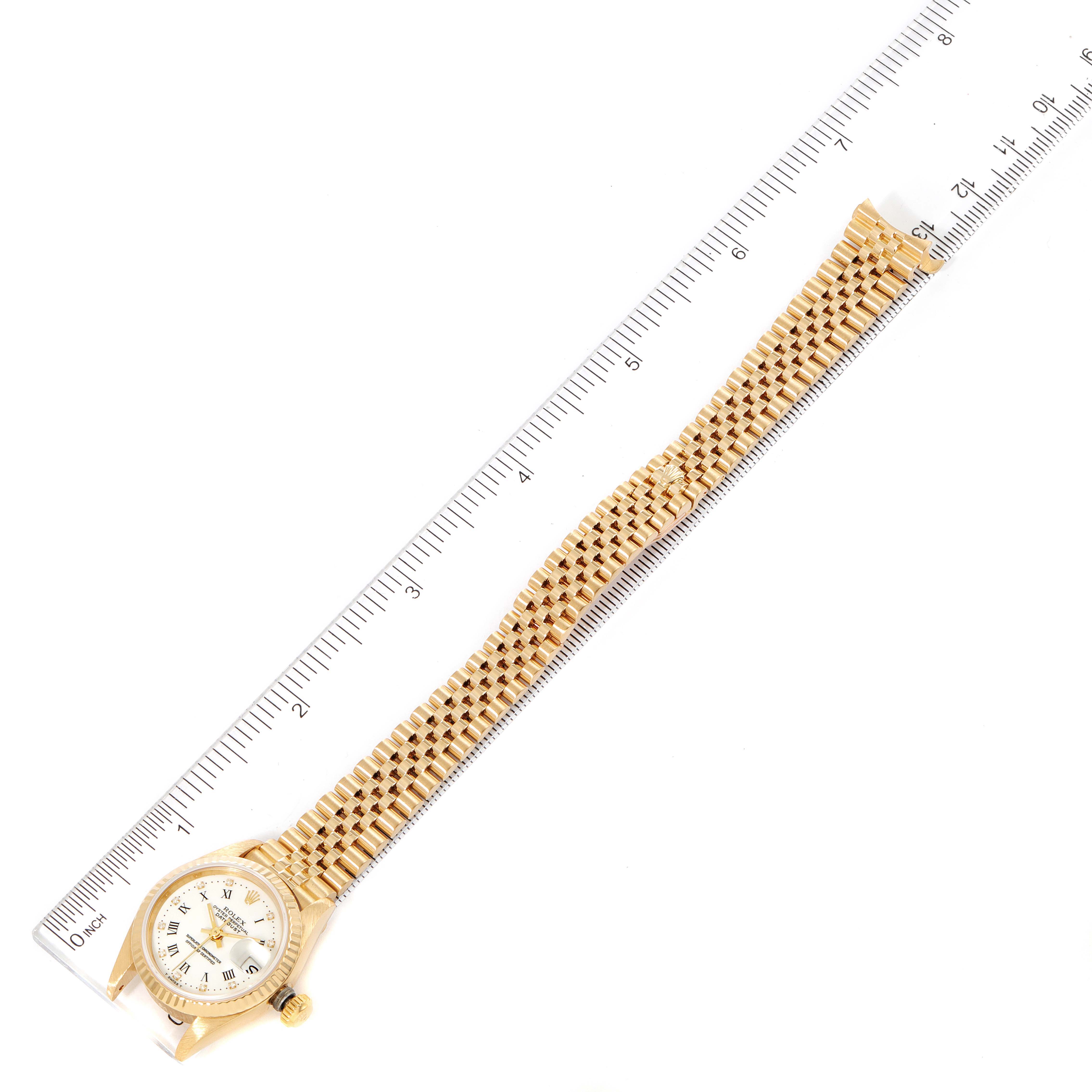 This image shows a Rolex President 69178 Women
s Yellow Gold White Dial 69178 Women
s Yellow Gold White Dial model watch laid flat, alongside a ruler for scale, displaying the bracelet and dial.