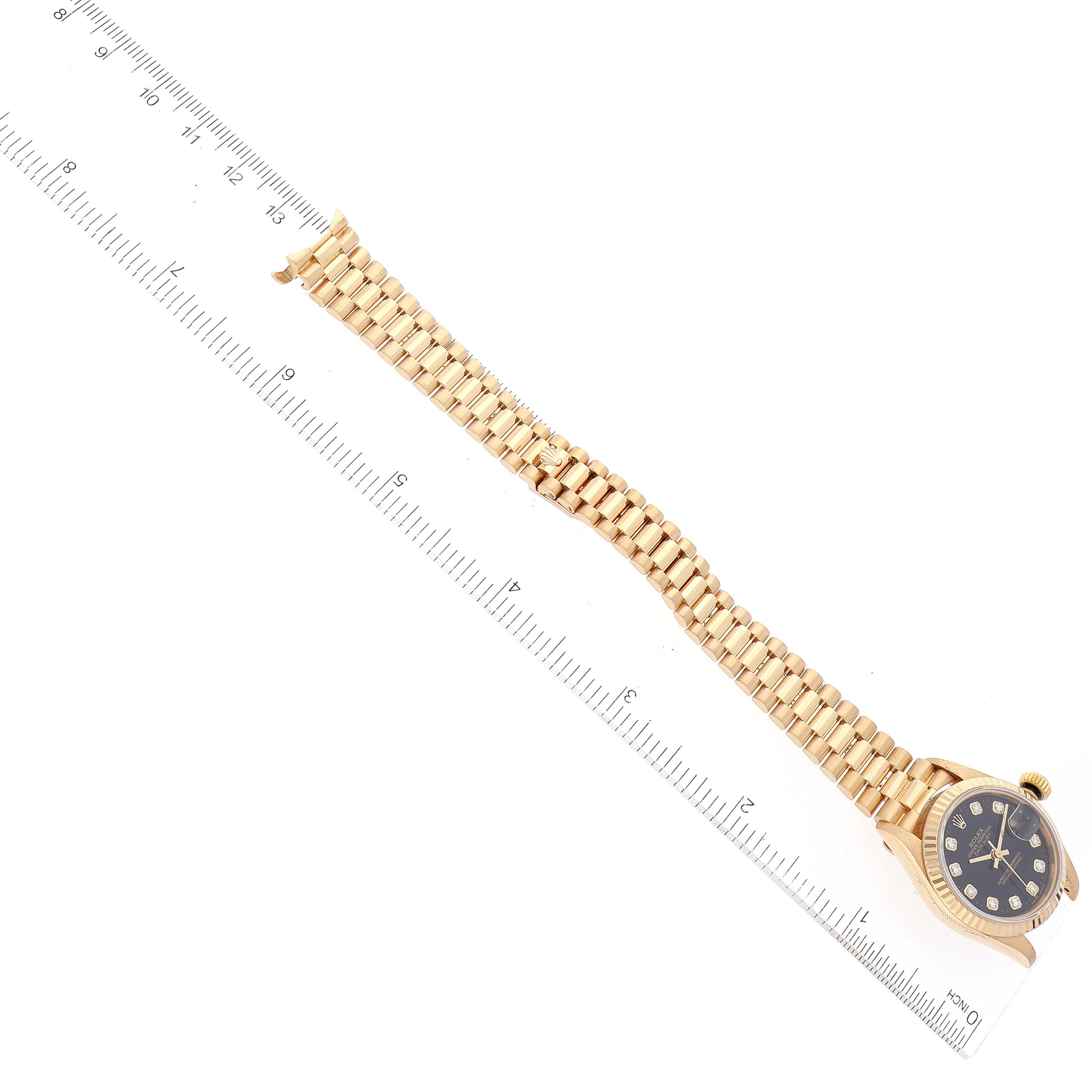 This overhead shot displays the face and bracelet of the Rolex President 79178 Women's Yellow Gold Black Dial 79178 Women's Yellow Gold Black Dial model watch, measured against a clear ruler.