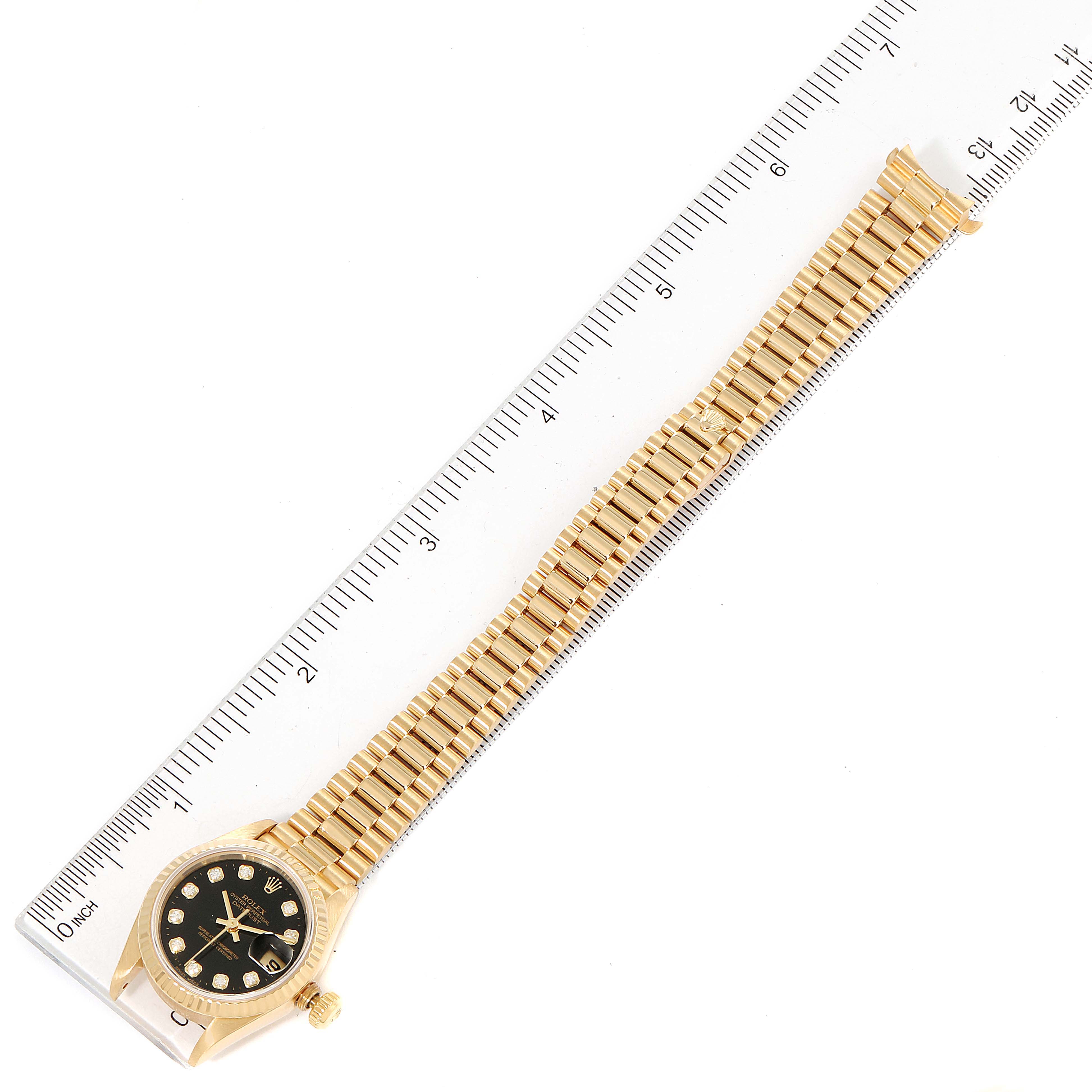 The Rolex President 79178 Women's Yellow Gold Black Dial 79178 Women's Yellow Gold Black Dial model watch is shown from a top-down angle, displaying its black dial, gold case, and bracelet along with a ruler for scale.