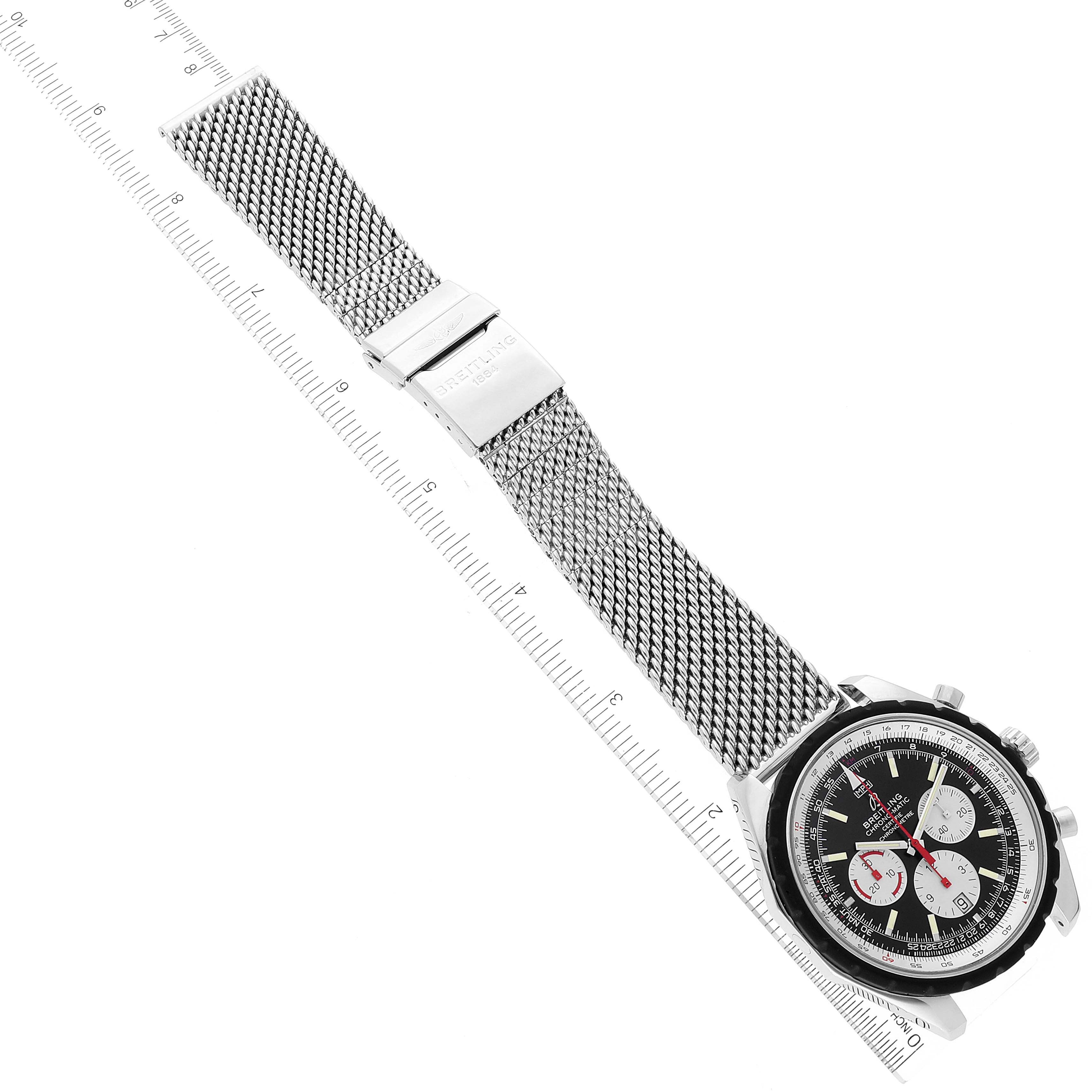 The image shows a Breitling Chronomatic A14360 Men's Stainless Steel Black Dial A14360 Men's Stainless Steel Black Dial watch angled diagonally, displaying its mesh strap, clasp, and face with a measuring scale beside it.