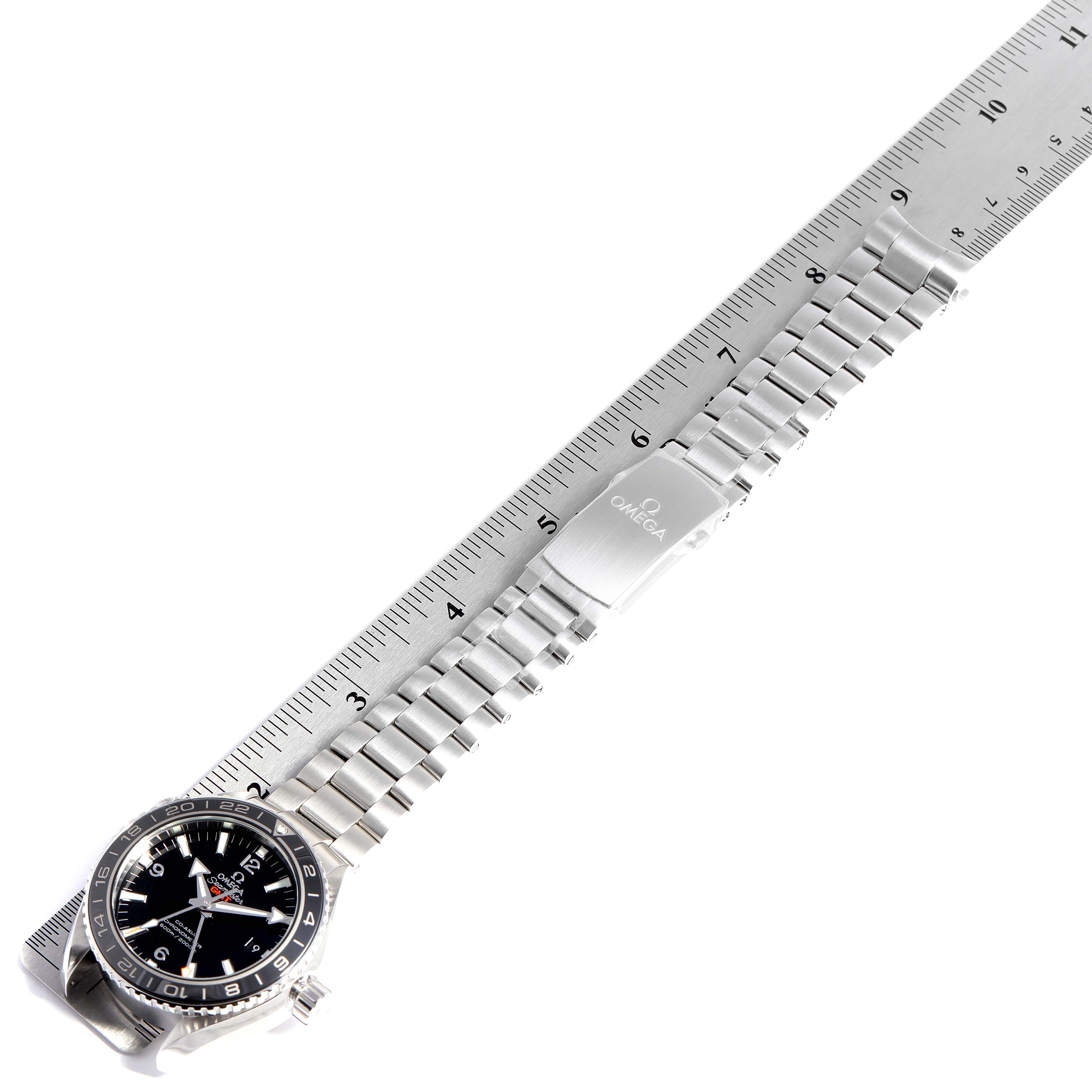 The image shows an overhead view of the Omega Planet Ocean 232.30.44.22.01.001 Men
s Stainless Steel Black Dial 232.30.44.22.01.001 Men
s Stainless Steel Black Dial watch, highlighting its face, bezel, stainless steel bracelet, and clasp laid alongside a ruler.