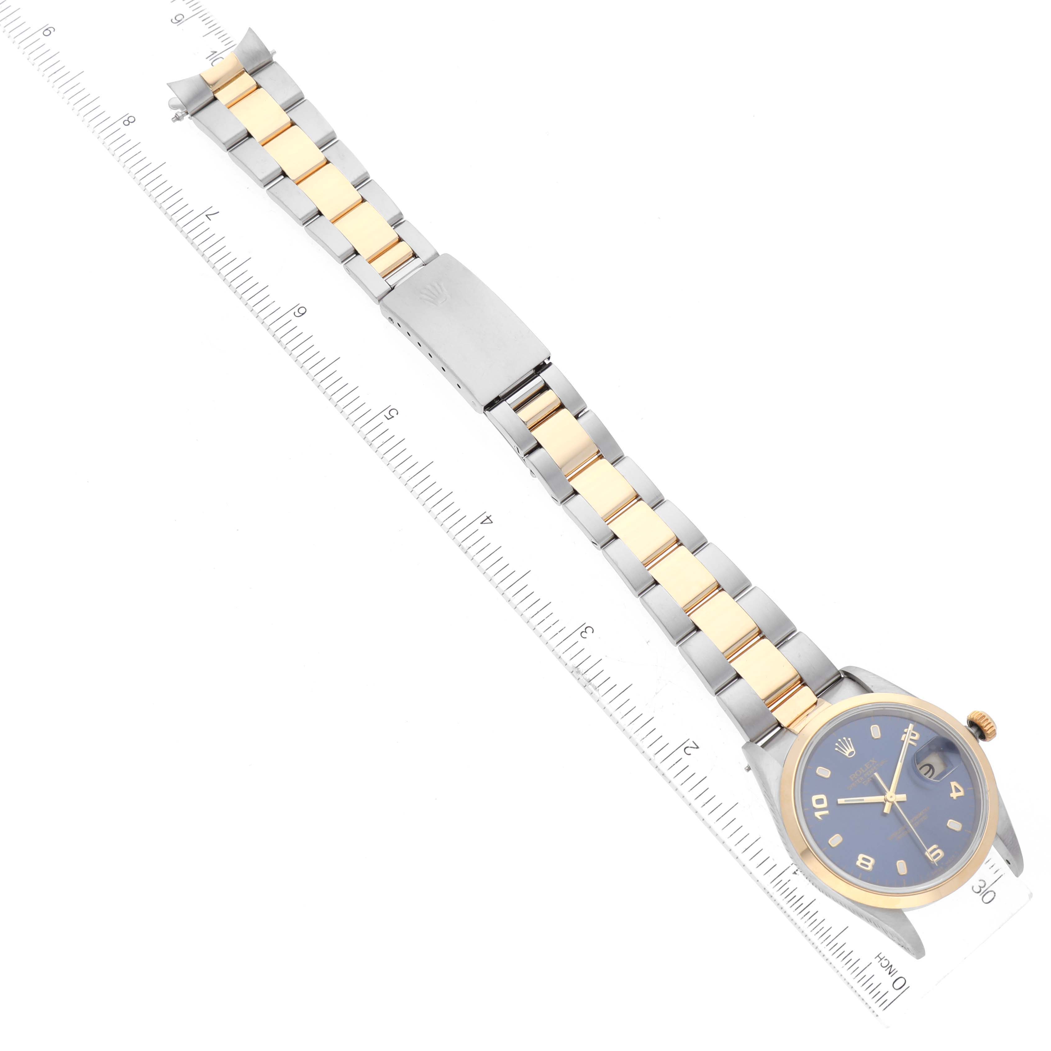 This image shows a Rolex Date 15203 Men
s Steel and Gold (two tone) Blue Dial 15203 Men
s Steel and Gold (two tone) Blue Dial model watch laid flat with its bracelet extended beside a ruler.