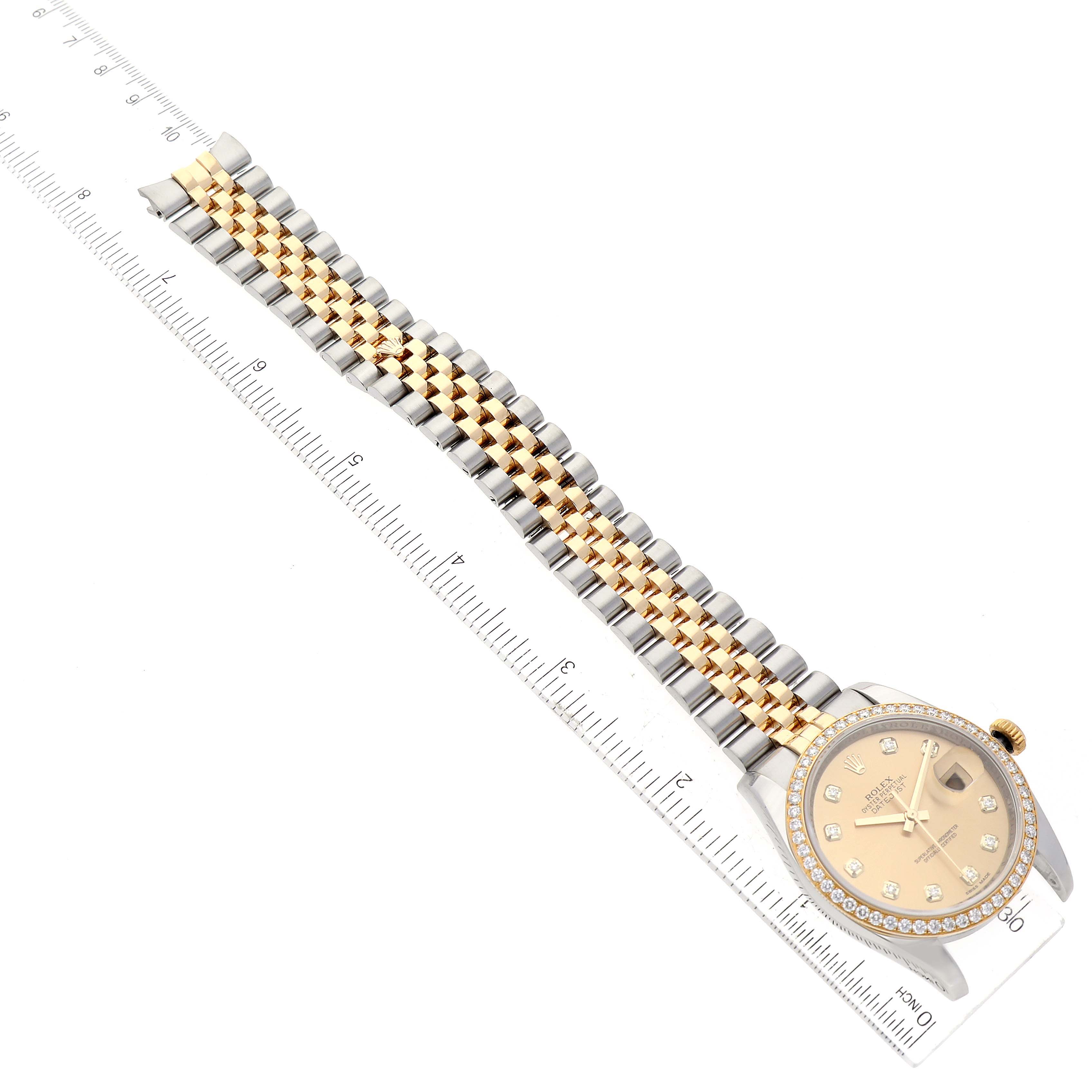 The Rolex Datejust 116243 Men's Steel and Gold (two tone) Champagne Dial 116243 Men's Steel and Gold (two tone) Champagne Dial watch is shown from an overhead angle, highlighting its face, bezel, and two-tone bracelet with a ruler for scale.
