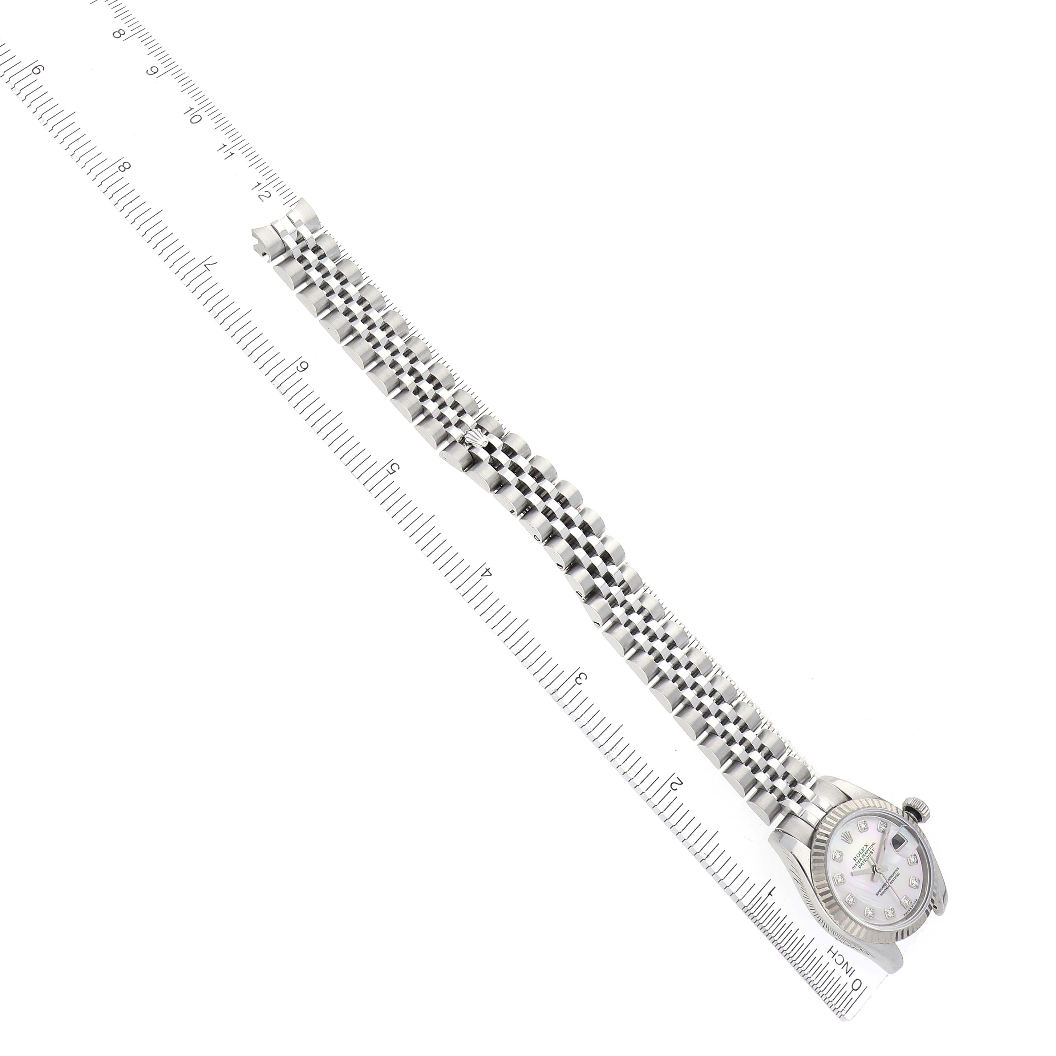 The Rolex Datejust 179174 Women
s Stainless Steel Mother of Pearl Dial 179174 Women
s Stainless Steel Mother of Pearl Dial watch is shown diagonally with the face, crown, and full bracelet visible alongside a ruler.