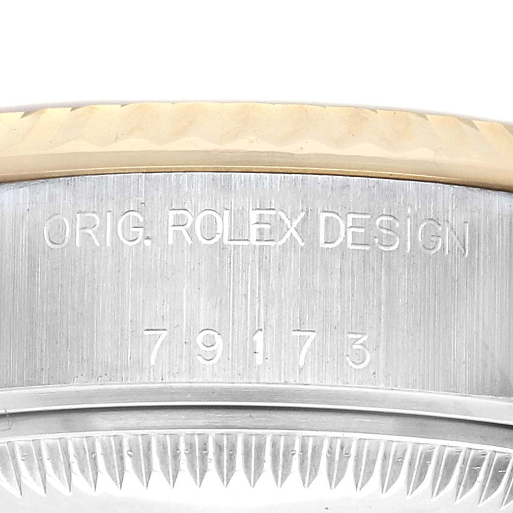 The image shows a close-up of the side view of a Rolex Datejust 79173 Women
s Steel and Gold (two tone) Champagne Dial 79173 Women
s Steel and Gold (two tone) Champagne Dial watch, highlighting the engraved model number and fluted bezel edge.