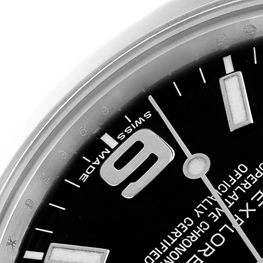 The image shows a close-up of a Rolex Explorer 214270 Men's Stainless Steel Black Dial watch face, highlighting the "9" numeral, markers, and partial text.