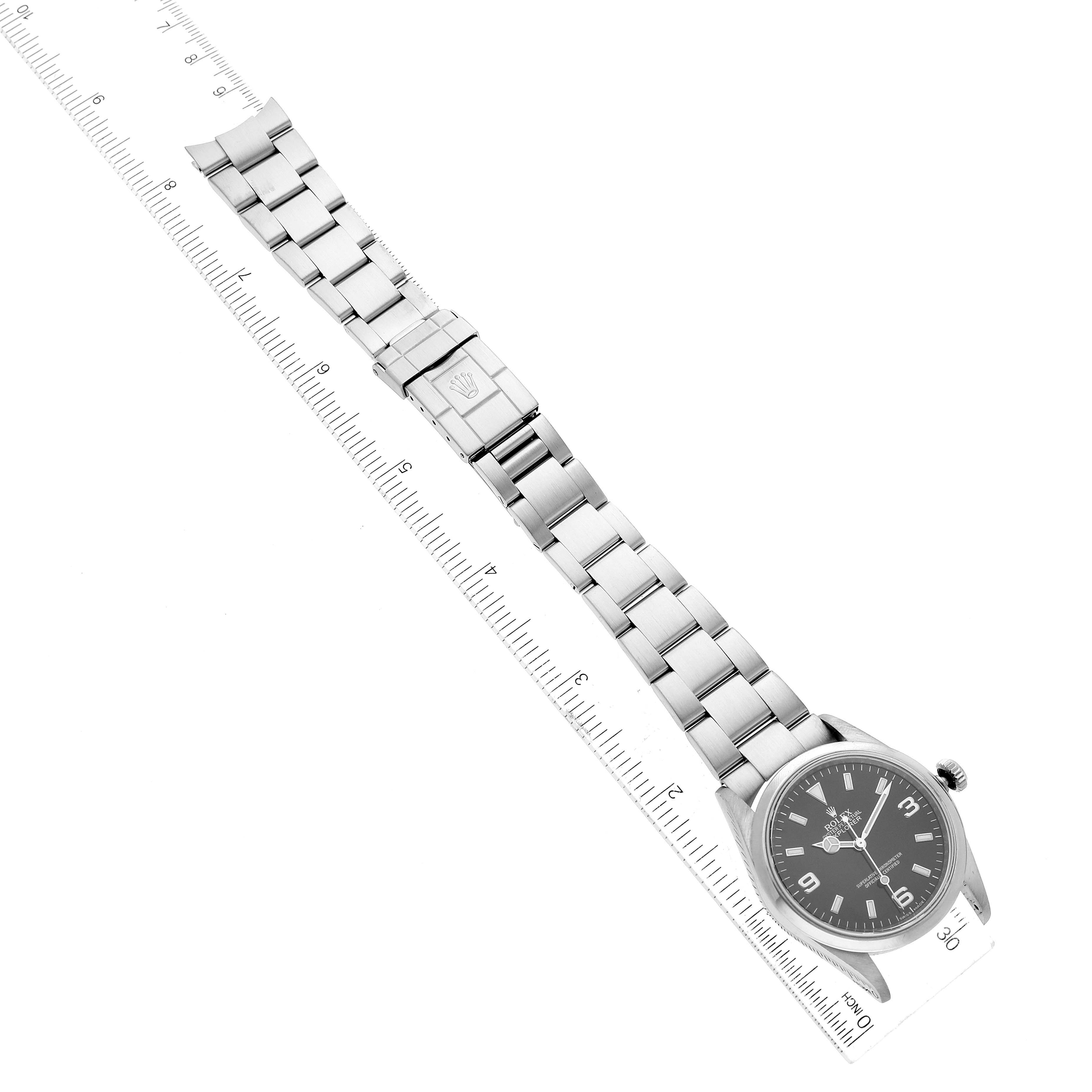 The Rolex Explorer 114270 Men
s Stainless Steel Black Dial 114270 Men
s Stainless Steel Black Dial watch is shown laid flat with a ruler for size reference, displaying its full bracelet and face.